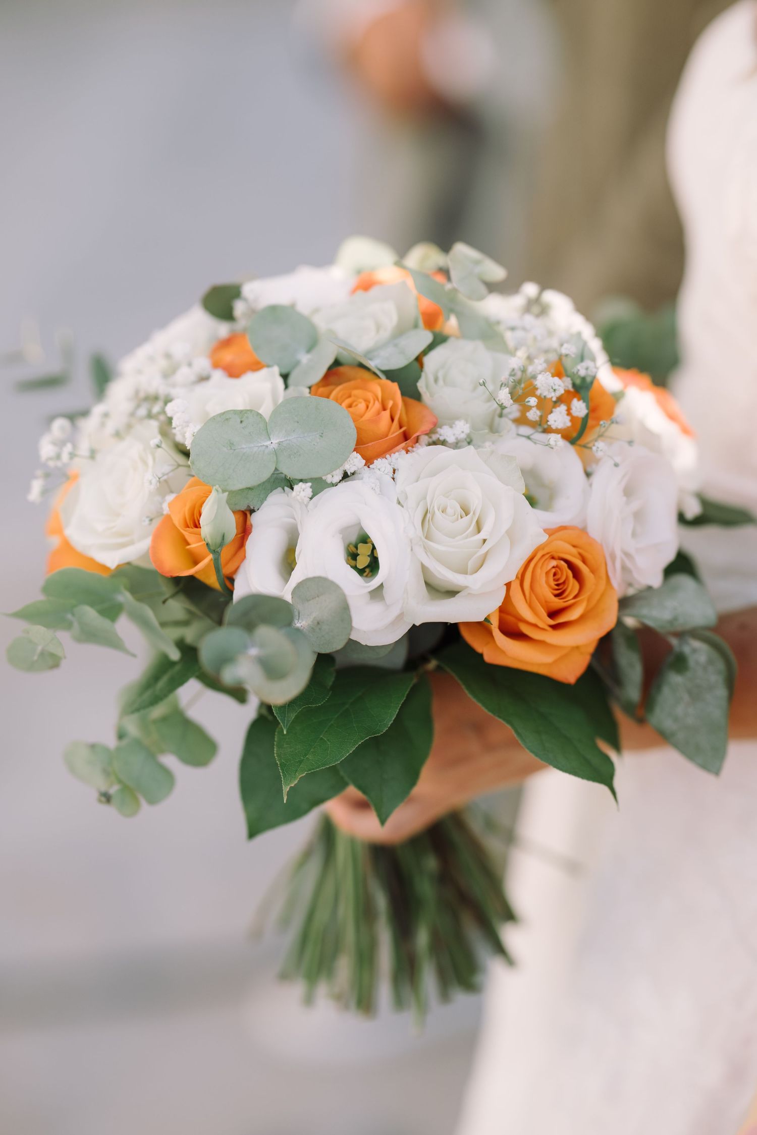 Bridal bouquet of white and orange roses with eucalyptus, held by the bride at a beach wedding
