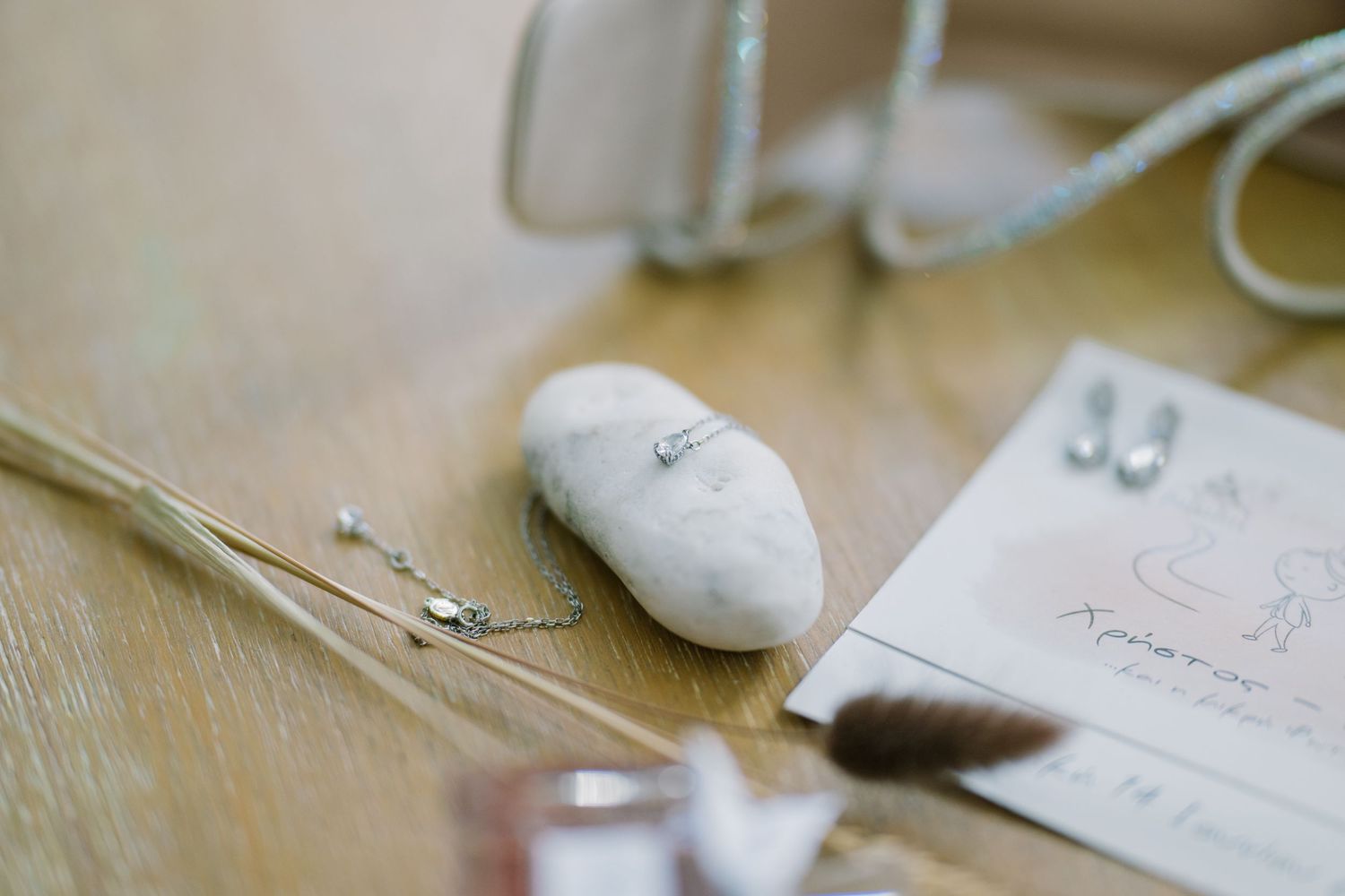 Bridal detail flat lay with a ring on a white pebble, earrings, dried grasses and a handwritten card