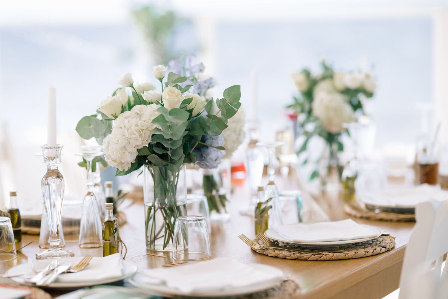 Wedding table with white flowers, eucalyptus and candles, styled for a seaside reception in Crete