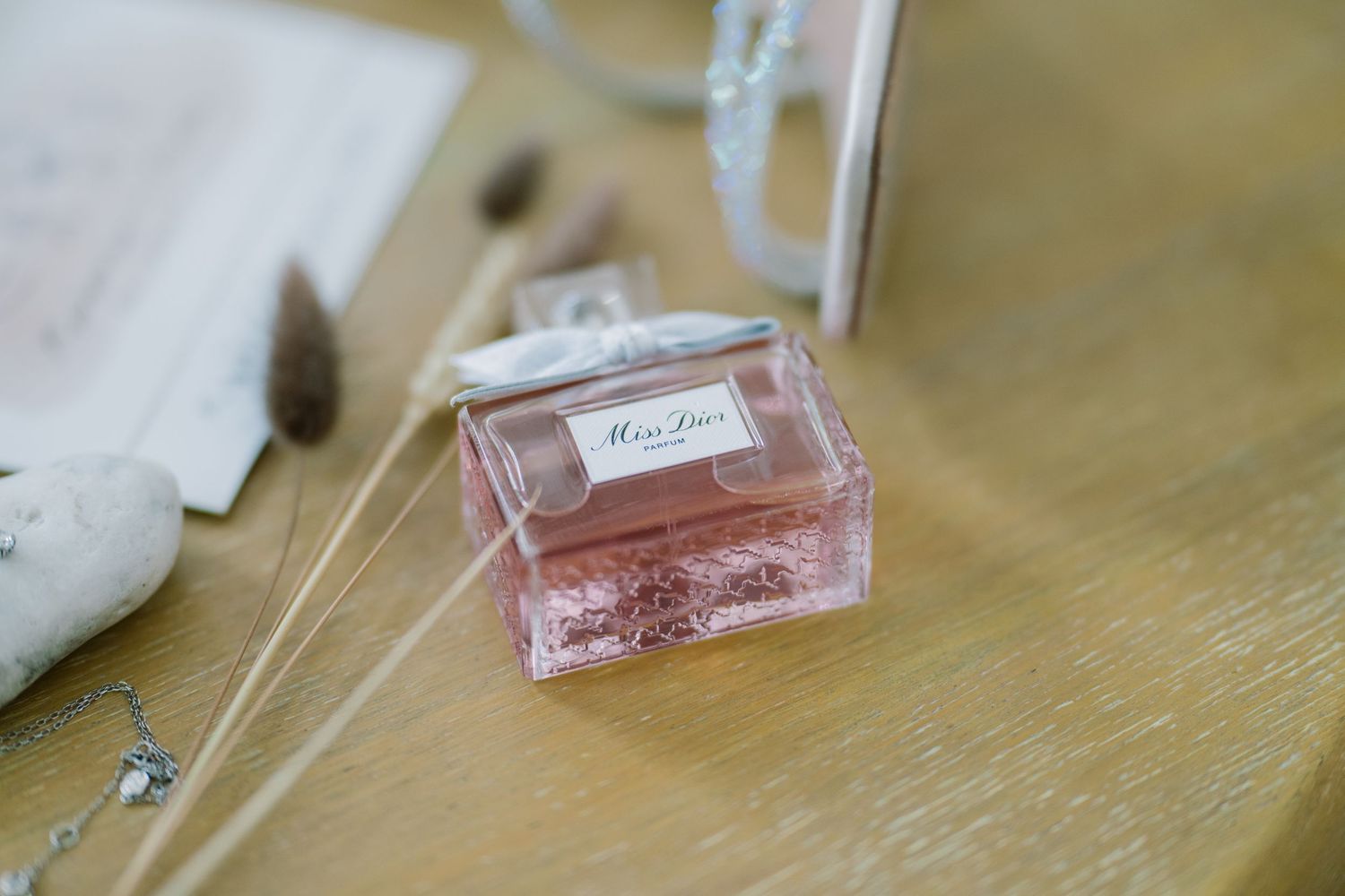 Perfume bottle among dried grasses, pebbles and stationery, elegant bridal preparation detail