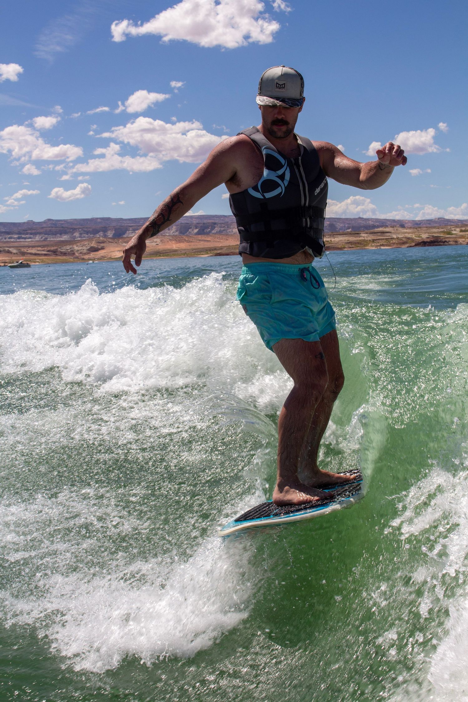Man wake surfing on turquoise water wearing a life vest and blue shorts on a sunny day at Lake Powell.