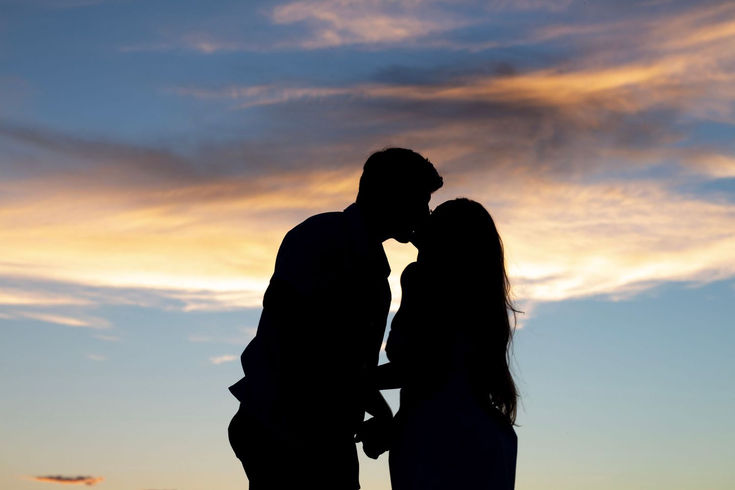 Romantic couple silhouette kissing against a vibrant sunset sky with colorful clouds at dusk.