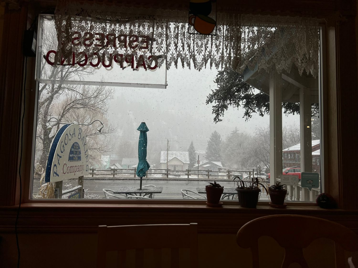 Cozy bakery window view of snowy winter landscape with espresso and cappuccino sign reflected in glass.