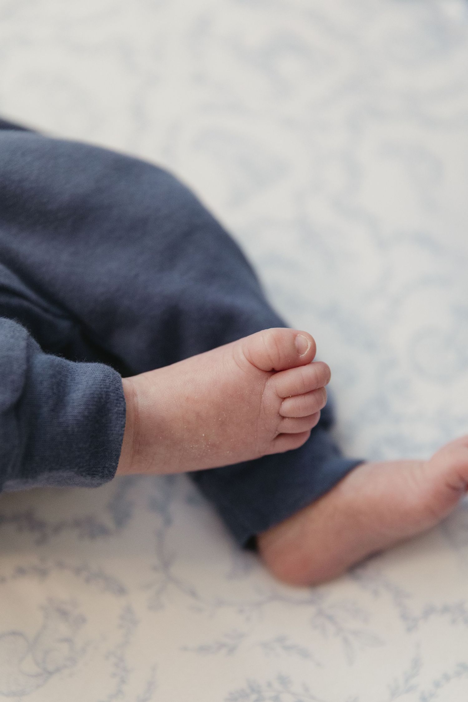 Close-up of tiny baby feet in blue pants resting on a soft patterned white blanket.