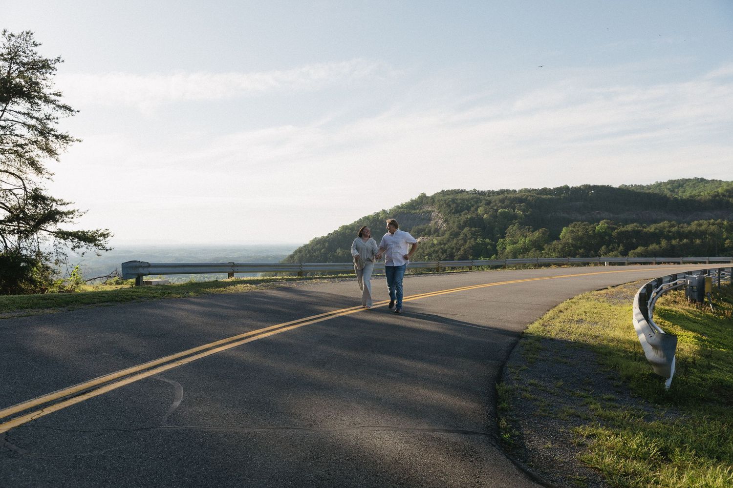 Two people jogging on a scenic winding road with lush green hills and ocean views on a clear sunny day.