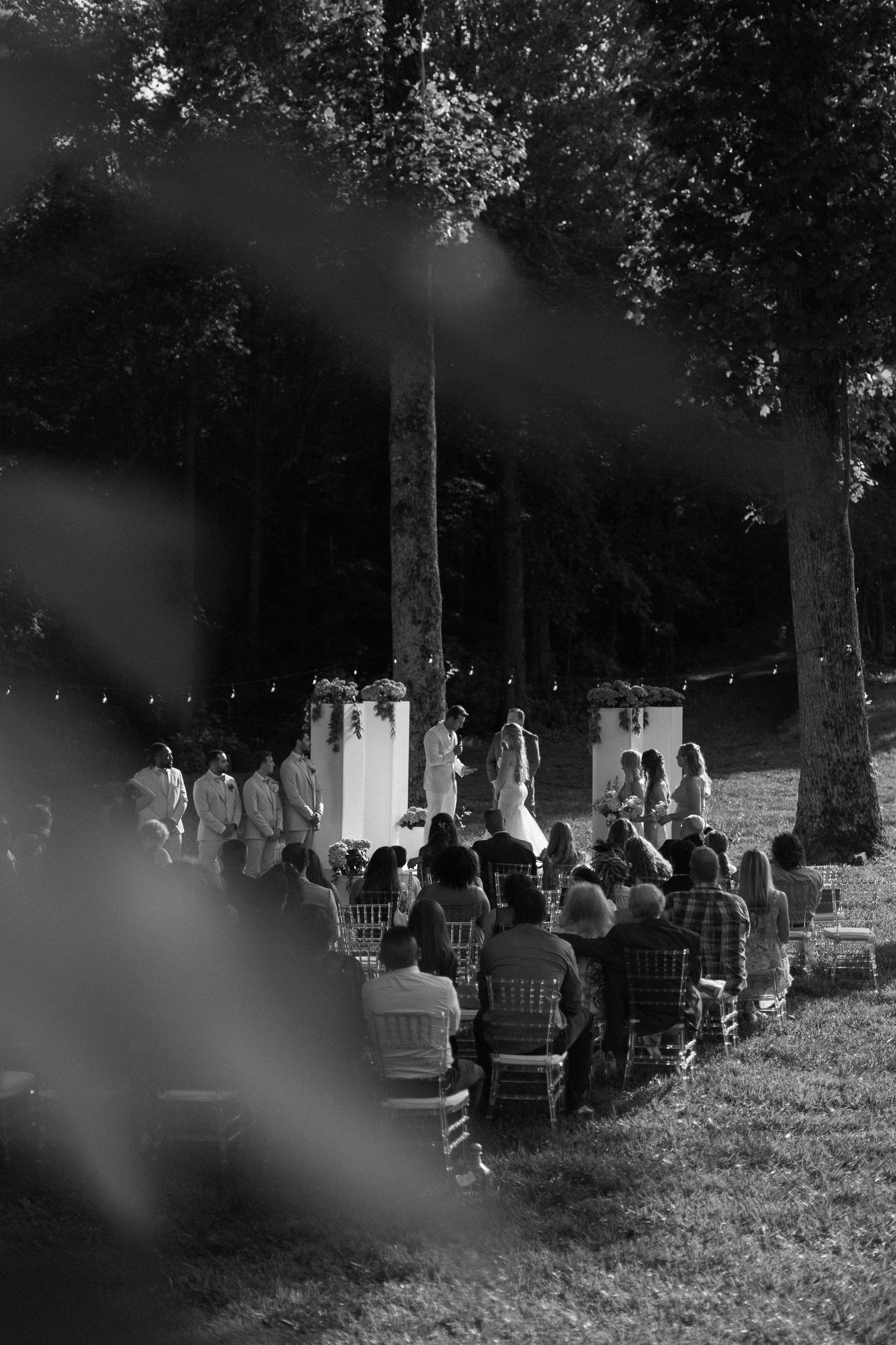 A black and white outdoor micro-wedding ceremony with guests seated in rows beneath tall trees in Blue Ridge Georgia