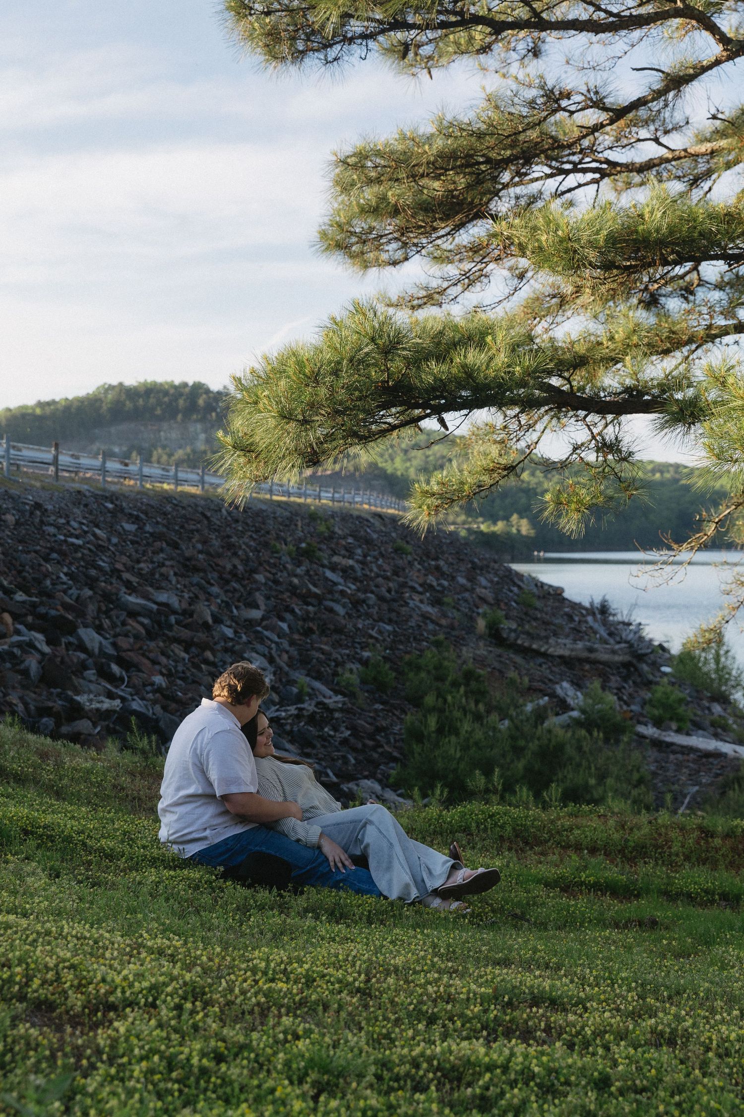 A couple sits peacefully on a grassy hillside overlooking the scenic carter's lake overlook surrounded by trees and rocky terrain