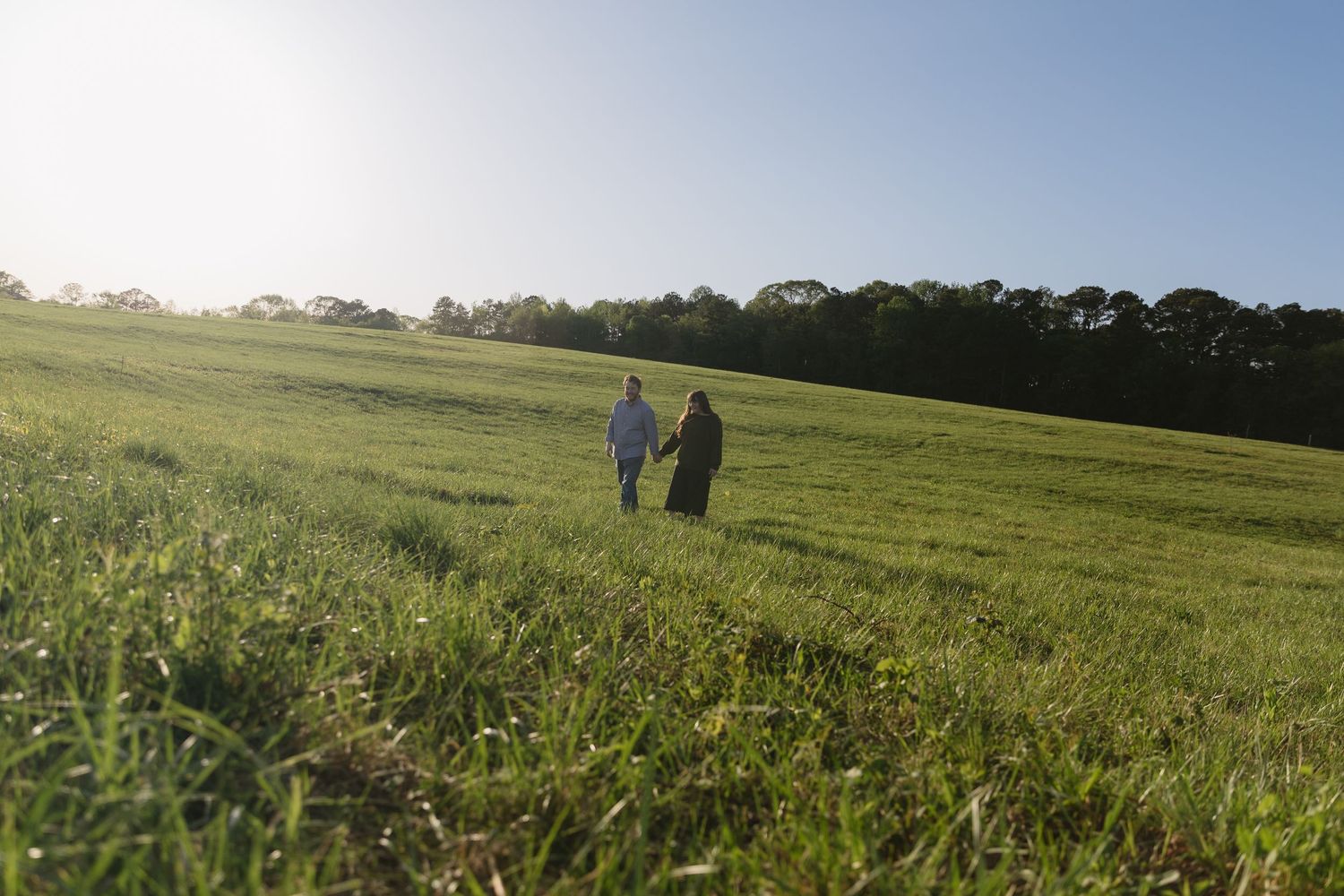 A couple hold hands walking through a field during golden hour. Photo taken by appalachian  elopement photographer Sydney Shepherd Photo.