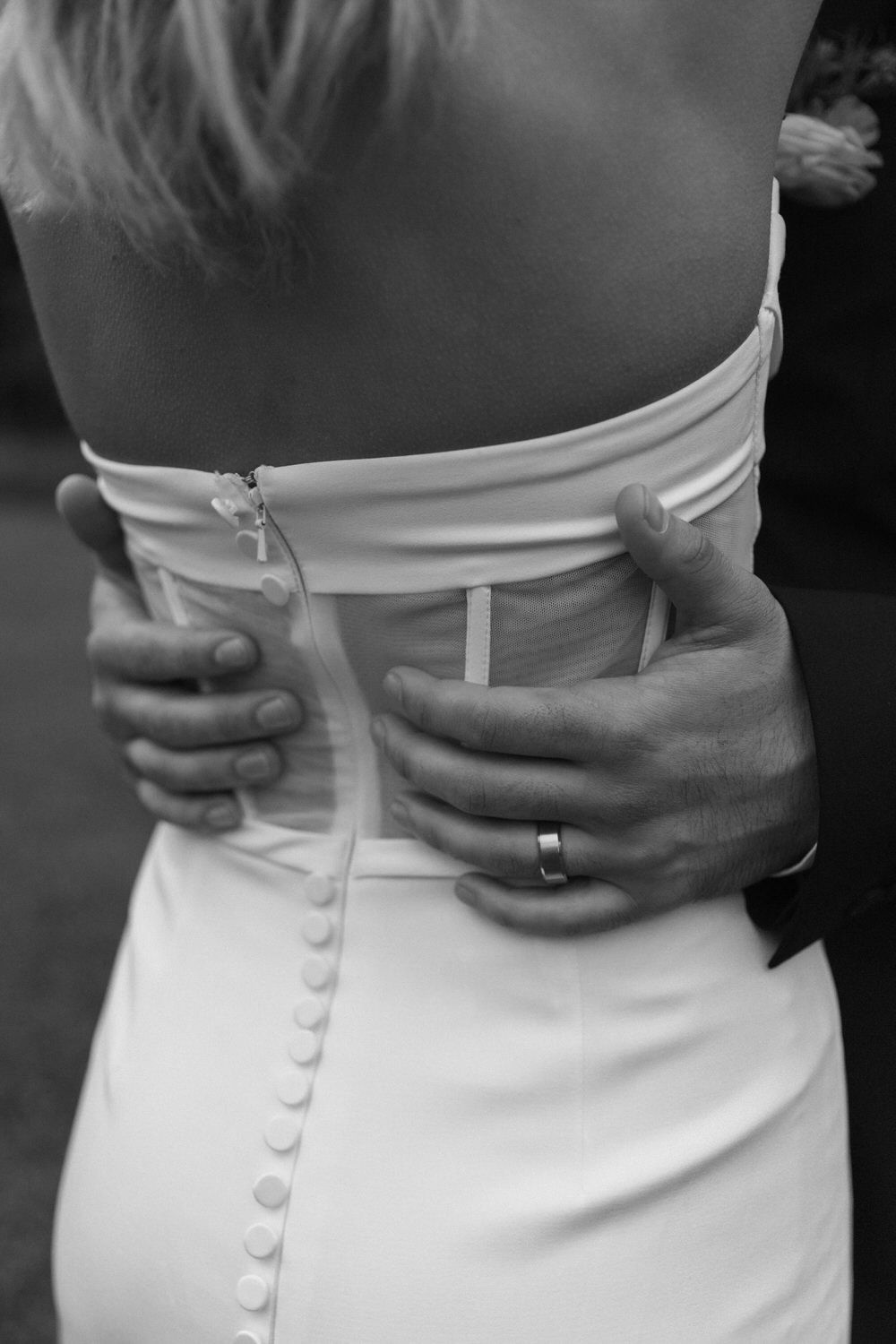 Black and white photo of grooms hands on the back of a wedding dress with delicate button details at North Georgia elopement