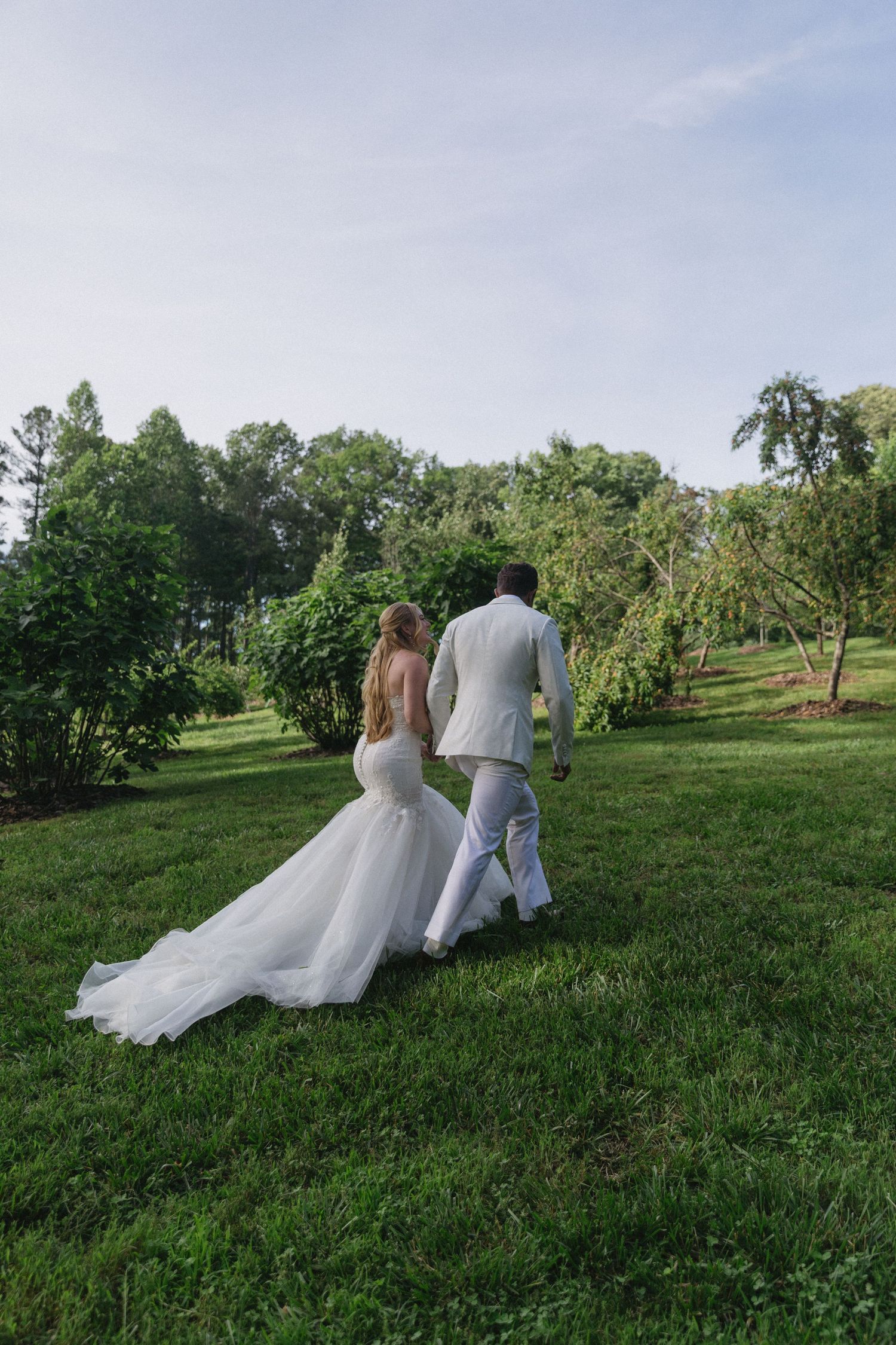 A couple walks hand in hand across a lush green hillside surrounded by trees on a summer elopement day in asheville north carolina