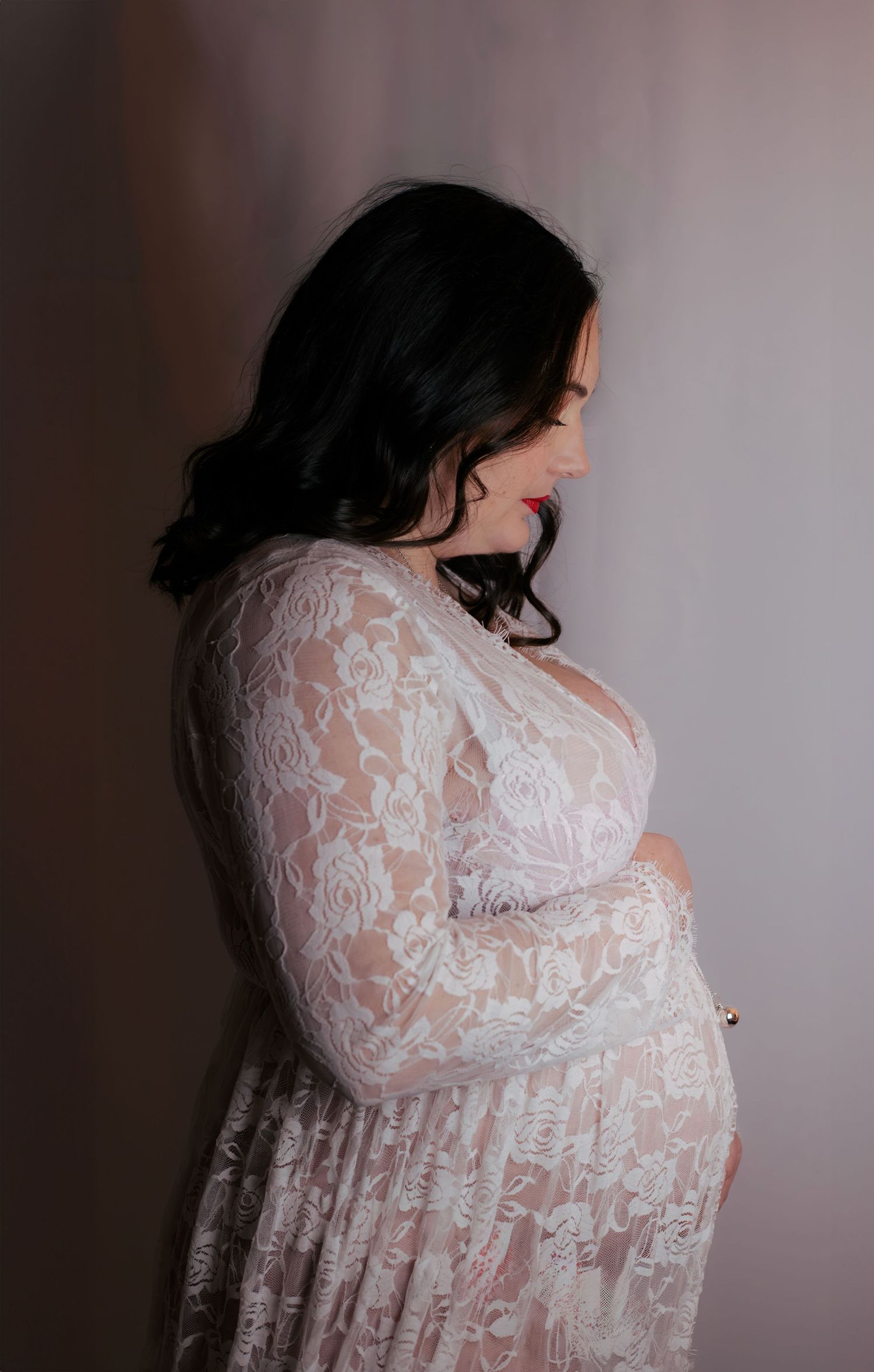 Séance grossesse Essonne 91, future maman en robe de dentelle blanche tenant son ventre avec tendresse, portrait maternité élégant