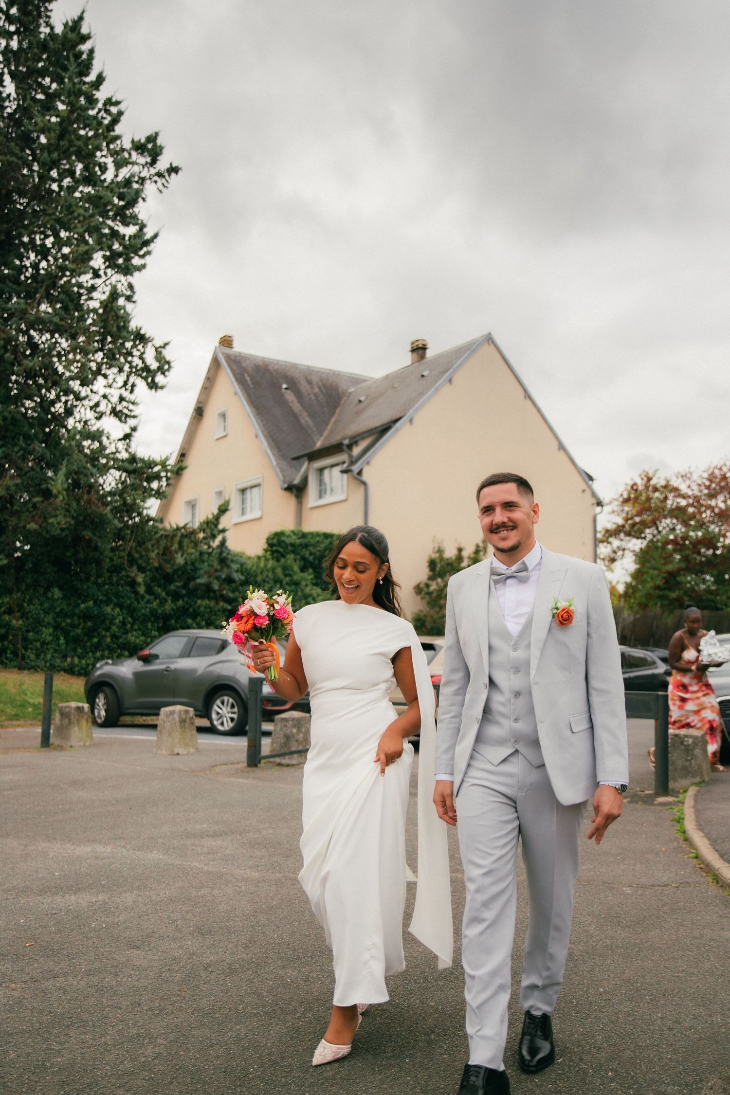Photographe mariage Essonne 91, mariés souriants et complices marchant main dans la main après la cérémonie, robe blanche et costume gris