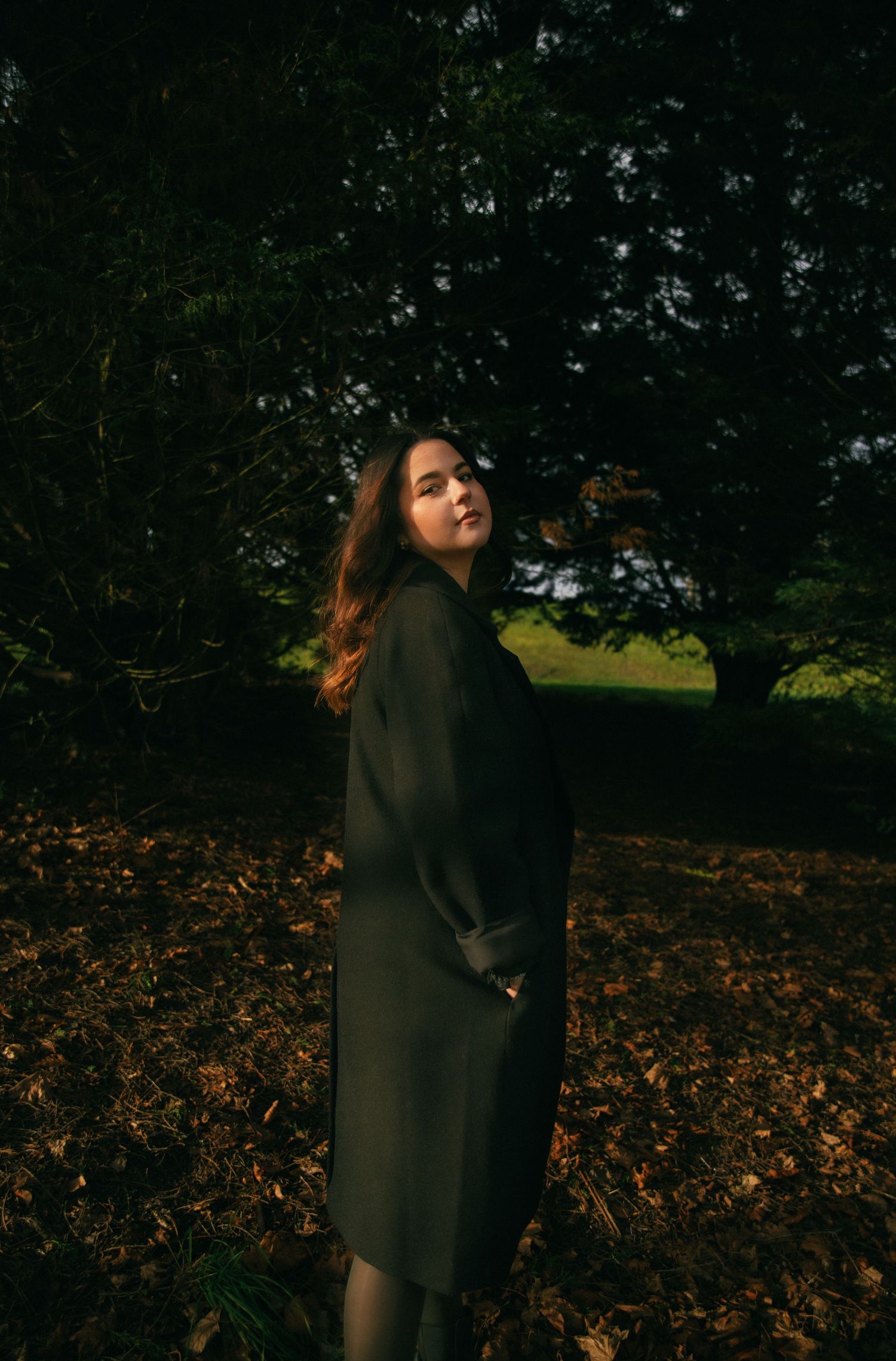 Photographe Essonne 91, portrait envoûtant jeune femme en manteau sombre se retournant dans une forêt automnale, photo lifestyle cinématique