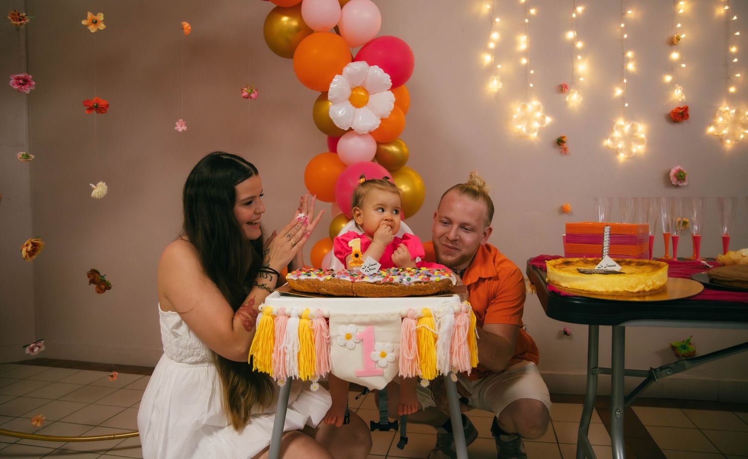 Parents admirant leur bébé devant son gâteau d'anniversaire, décor de ballons colorés et guirlandes lumineuses. Reportage famille Essonne 91