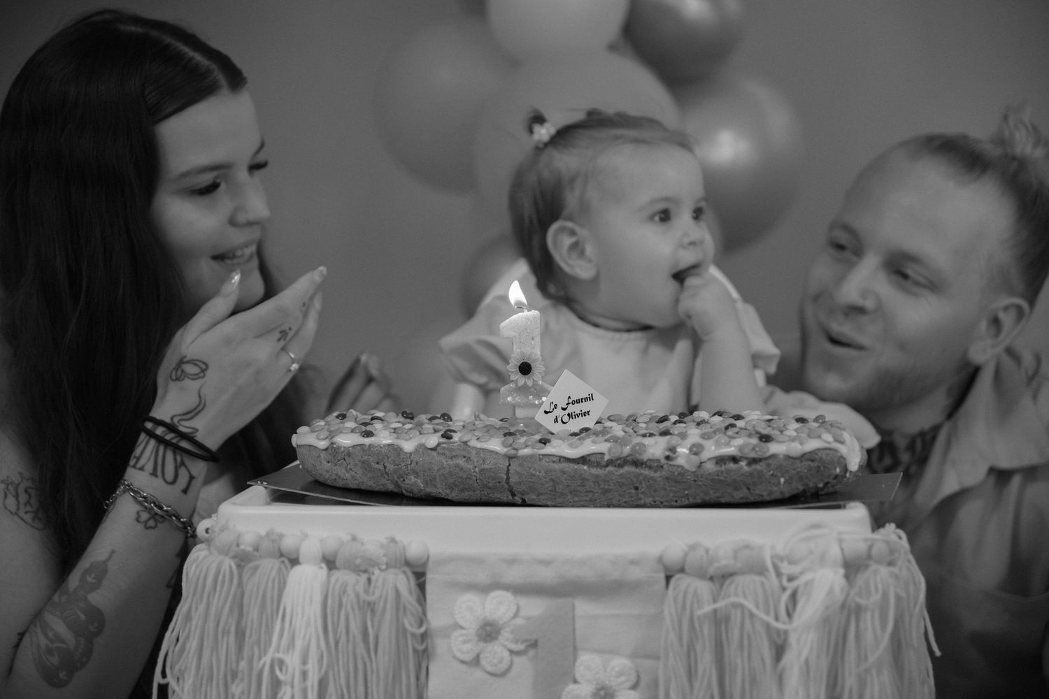Portrait famille Essonne 91, bébé découvrant son gâteau de premier anniversaire entouré de ses parents complices, noir et blanc émouvant