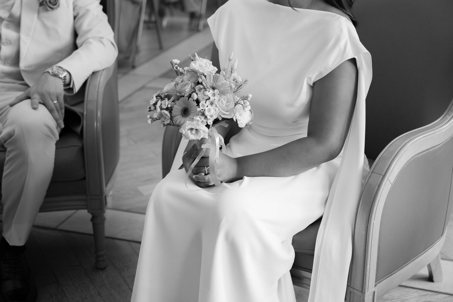 Mariée assise en noir et blanc, robe élégante et bouquet de fleurs champêtres entre les mains. Reportage mariage en Essonne. Photographe 91.