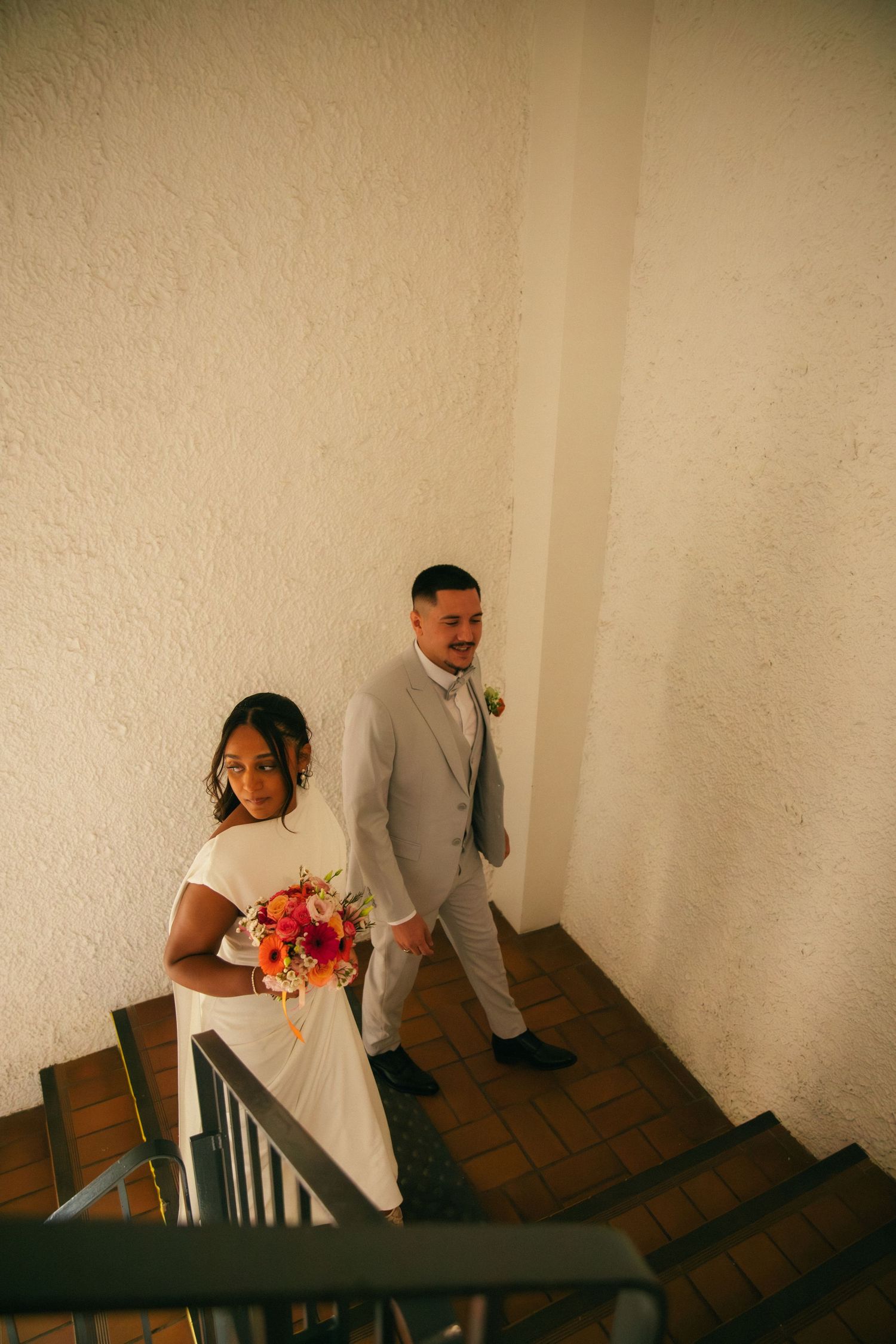 Photographe mariage Essonne 91, mariés dans un escalier vus en plongée, mariée au bouquet coloré et marié en costume gris, reportage mariage
