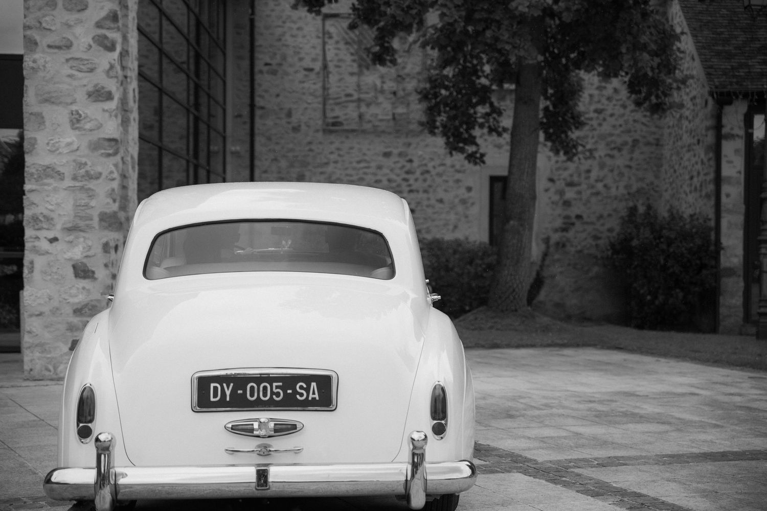 Photographe mariage Essonne 91, voiture de collection blanche devant un domaine en pierre, noir et blanc, détail reportage mariage chic