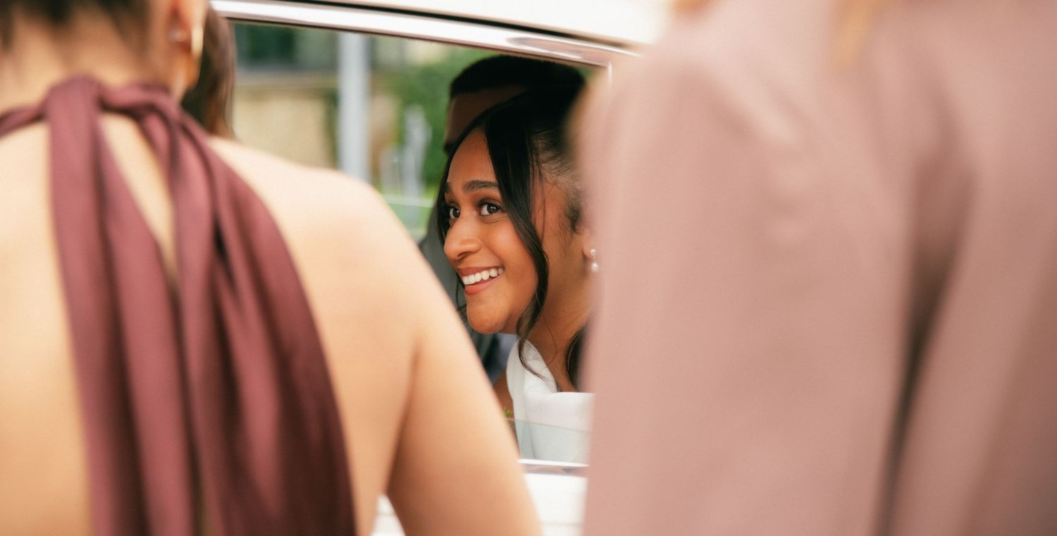 Photographe mariage Essonne 91, mariée souriante et radieuse reflétée dans le miroir d'une voiture, entourée de ses demoiselles d'honneur