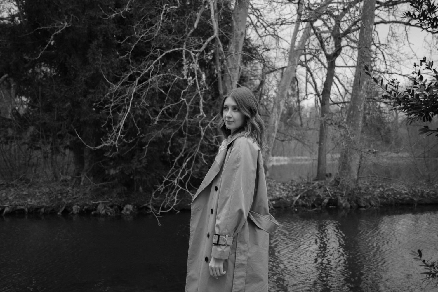 Photographe Essonne 91, portrait jeune femme en trench camel se retournant au bord d'un lac en forêt hivernale, séance photo lifestyle