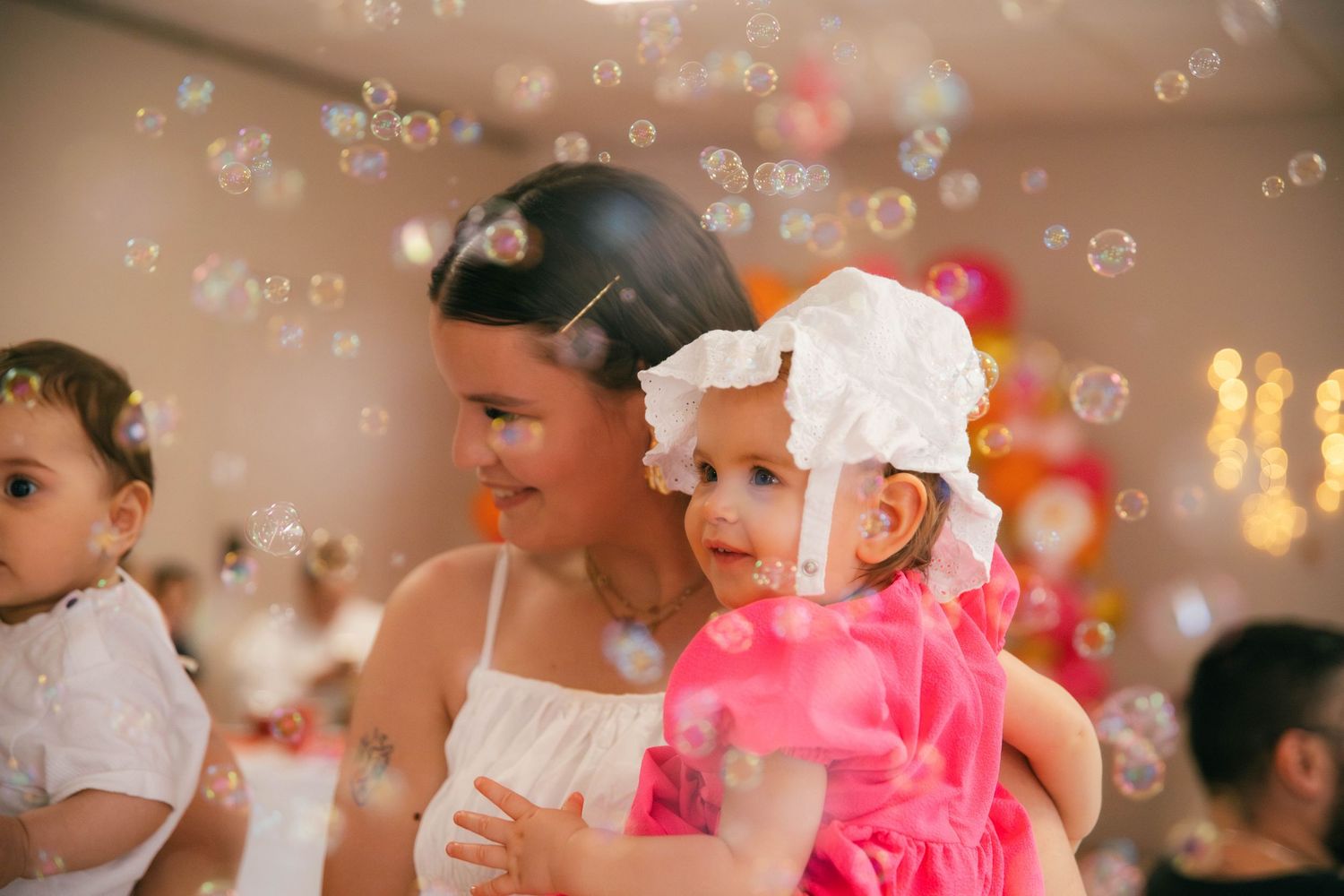 Jeune fille tenant un bébé entourés de bulles de savon lors d'un anniversaire festif. Reportage famille en Essonne. Photographe événement 91