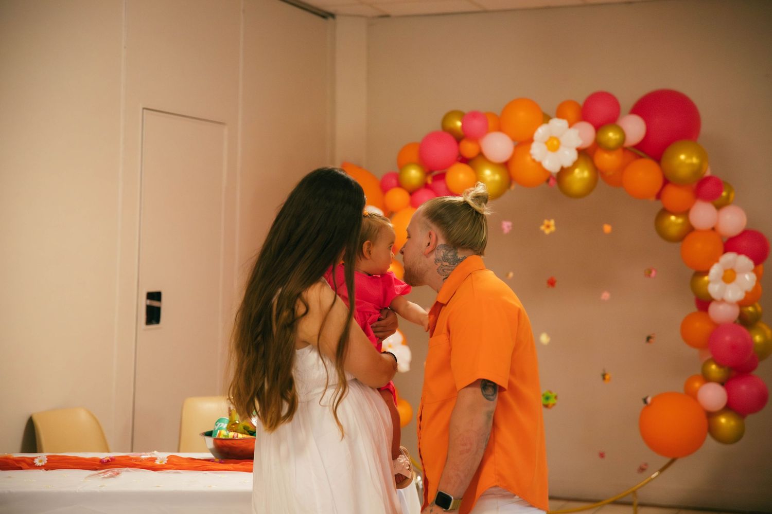 Séance photo famille complice, parents et bébé s'embrassant tendrement devant une arche de ballons colorés, photographe famille Essonne 91