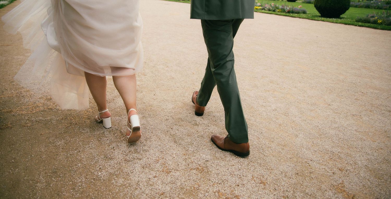 Photographe mariage Essonne 91, mariés marchant côte à côte dans un parc, robe blanche et costume vert, reportage mariage naturel et élégant