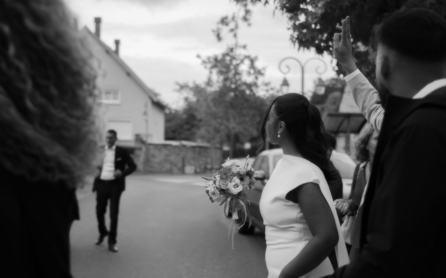 Mariée en noir et blanc saluant ses invités devant l'église, bouquet à la main, ambiance authentique. Reportage mariage Essonne. Photographe