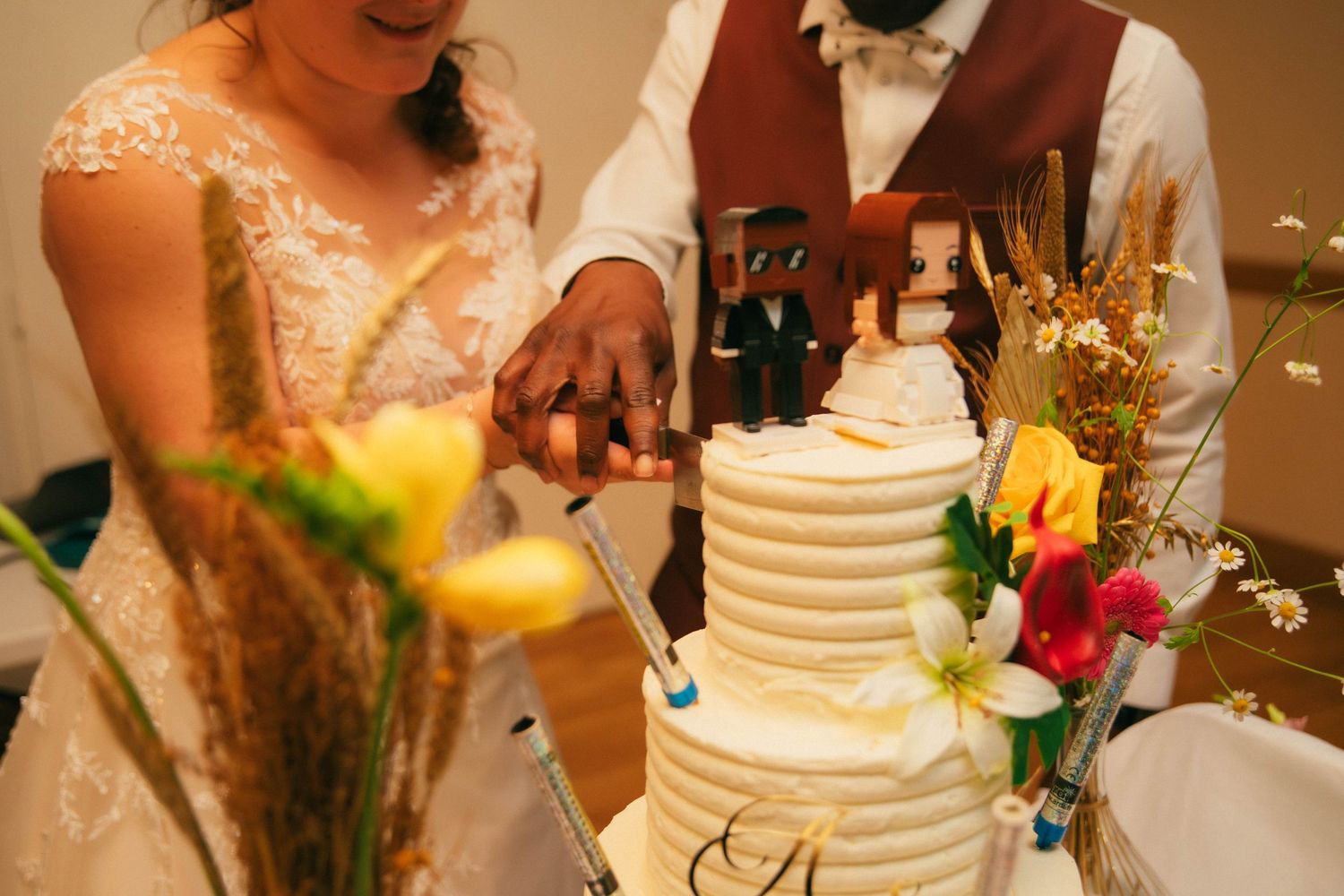 Mariés coupant leur wedding cake à étages décoré de fleurs colorées et épis de blé. Reportage mariage en Essonne. Photographe mariage 91.
