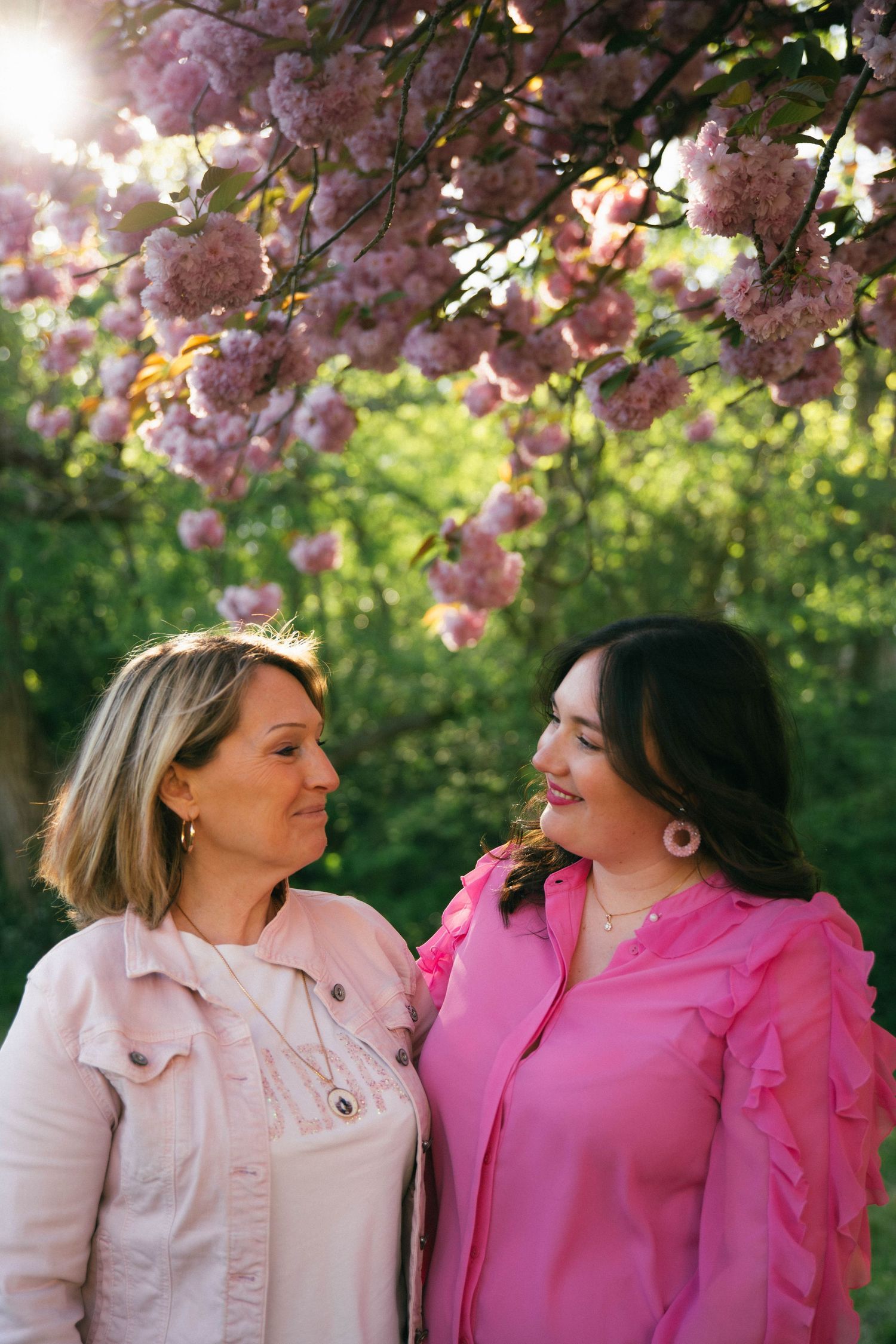 Photographe Essonne 91, deux femmes complices se regardant en souriant sous un cerisier en fleurs rose, séance photo lumineuse