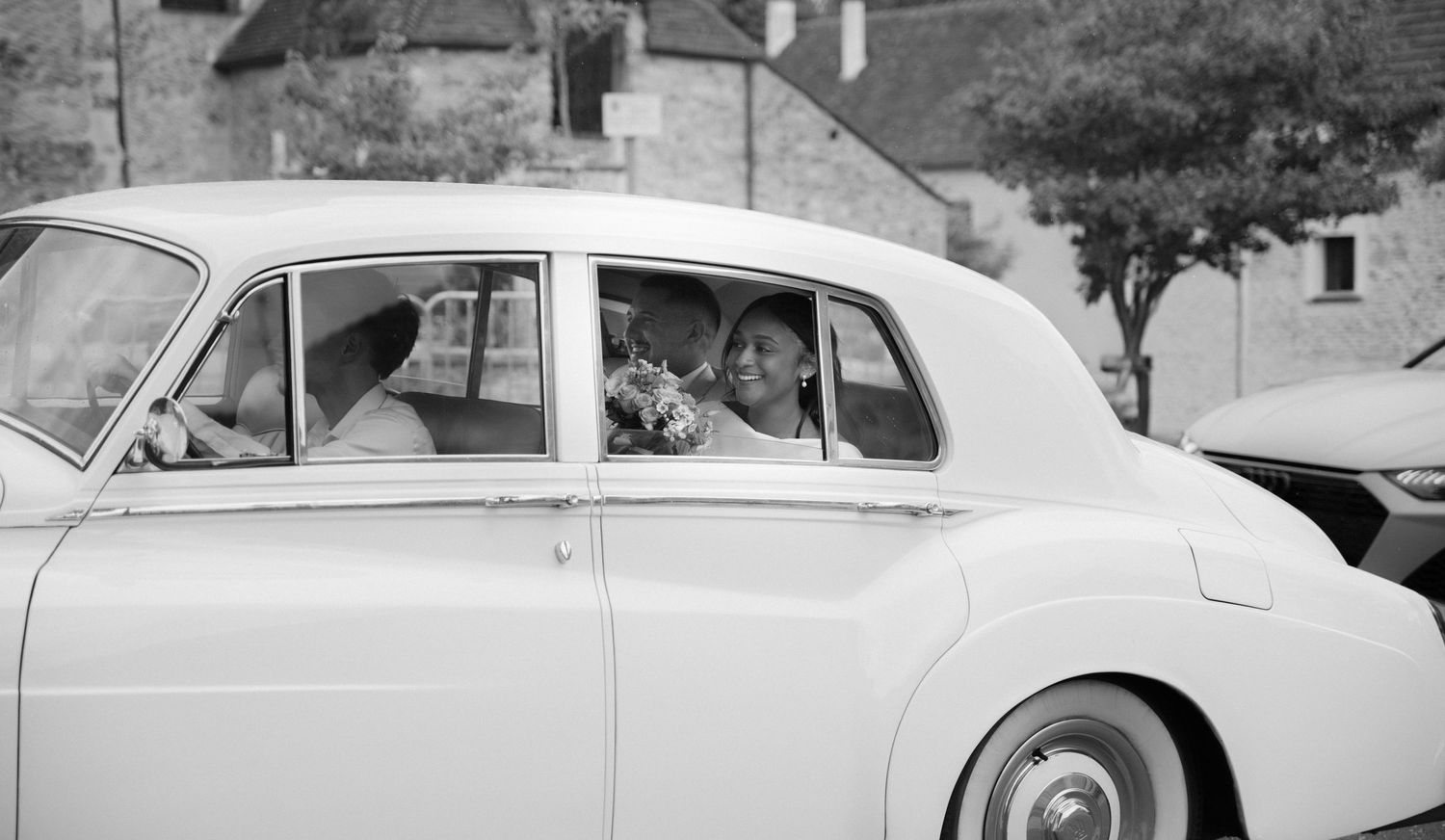 Photographe mariage Essonne 91,mariée et accompagnatrice souriantes dans une voiture de collection blanche, noir et blanc, reportage mariage