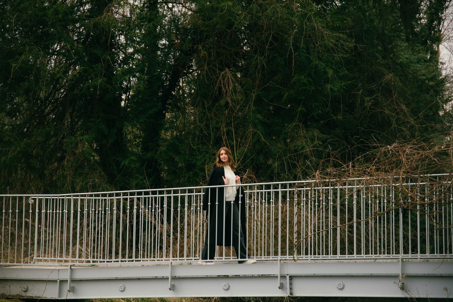 Portrait d'une femme sur une passerelle métallique entourée de végétation, pose naturelle et élégante. Séance portrait Essonne. Photographe