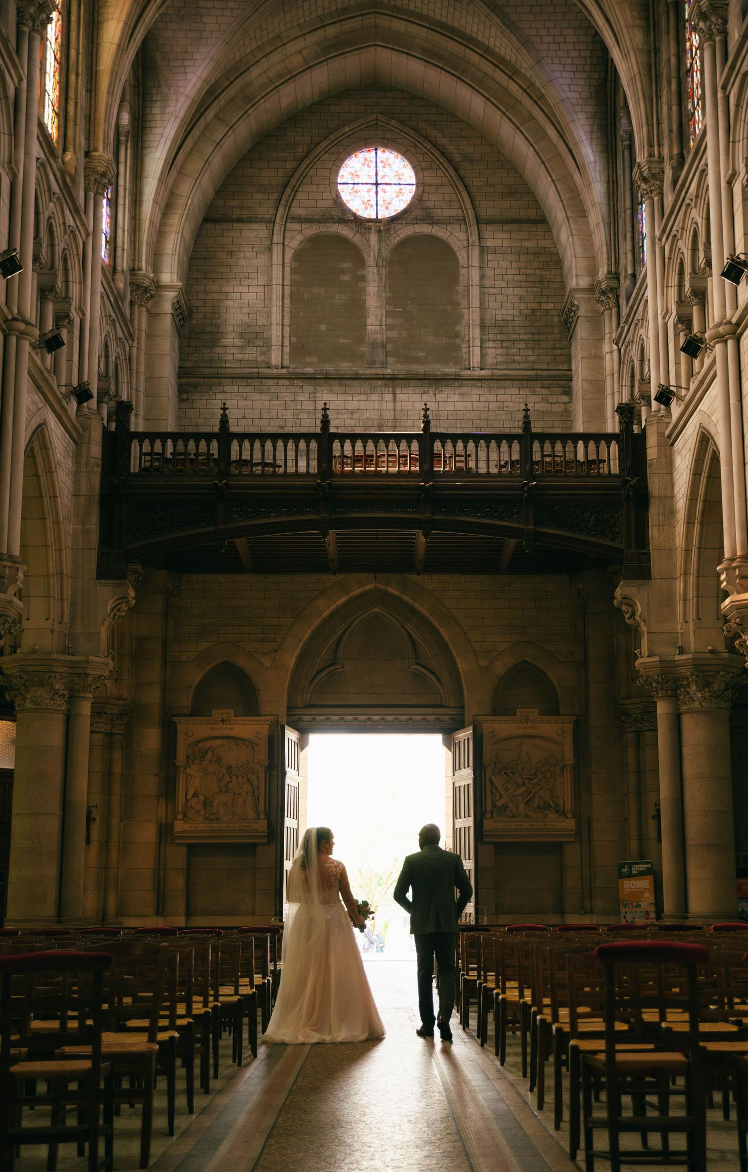 Photographe mariage Essonne 91, mariés de dos dans l'allée centrale d'une église face à la lumière, cérémonie religieuse, reportage mariage
