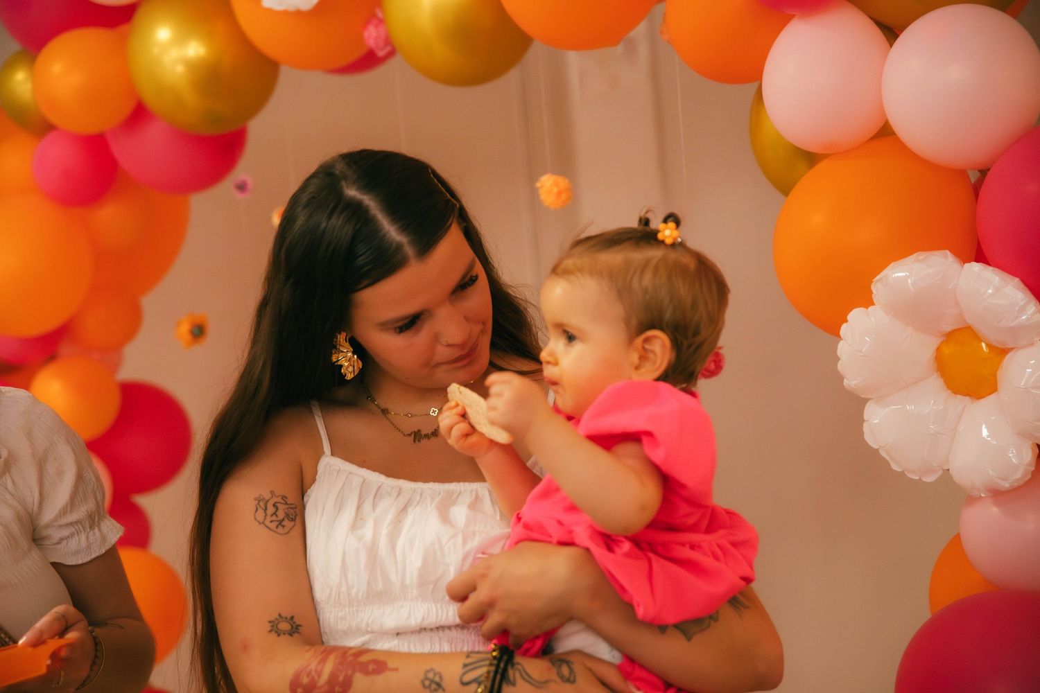 Complicité mère-enfant Essonne 91, maman tenant son bébé en robe rose sous une arche de ballons colorés, séance anniversaire douce