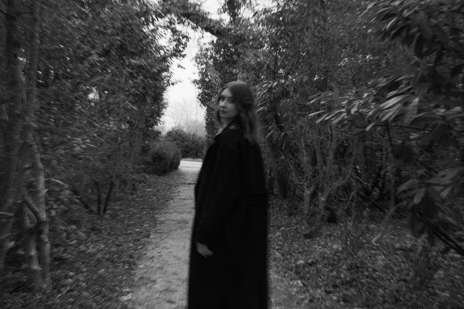 Portrait en noir et blanc d'une femme dans un sentier boisé, ambiance poétique et mystérieuse. Séance photo en extérieur Essonne, 91.