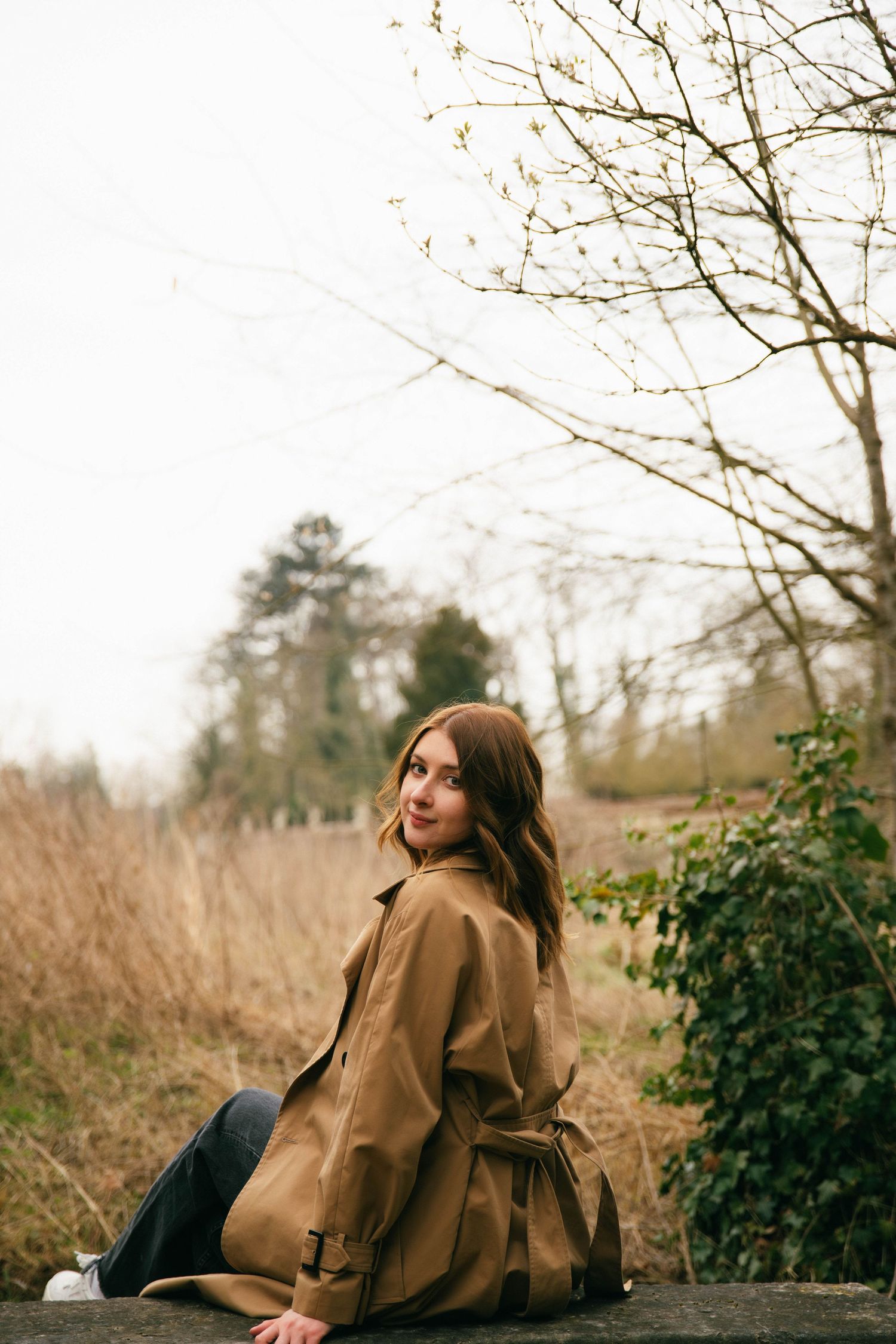 Portrait féminin Essonne 91, jeune femme en trench camel souriante assise dans la nature hivernale, séance photo lifestyle naturelle