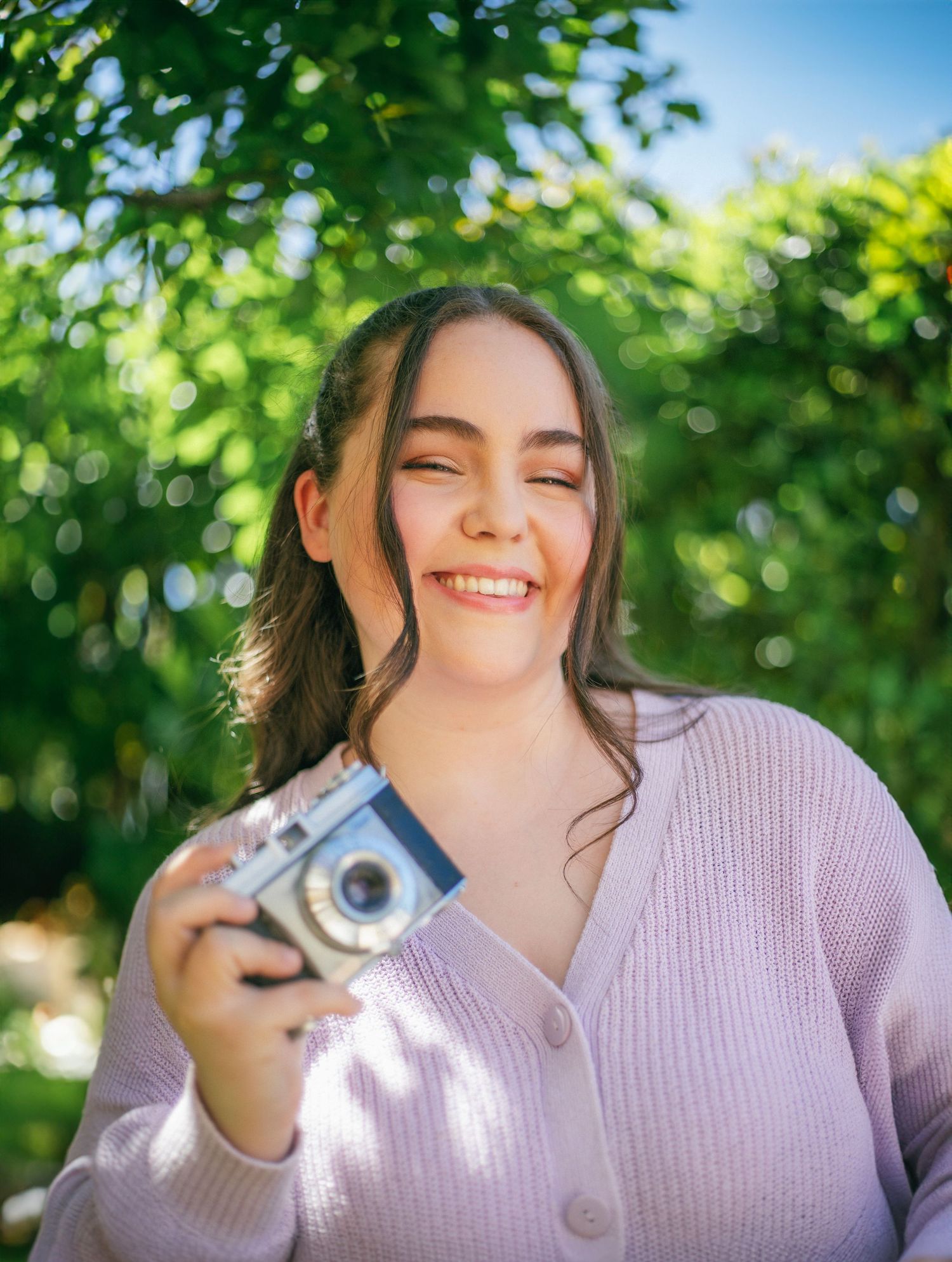 Photographe Essonne 91, jeune femme souriante tenant un appareil photo argentique en plein air, séance photo portrait lifestyle naturel