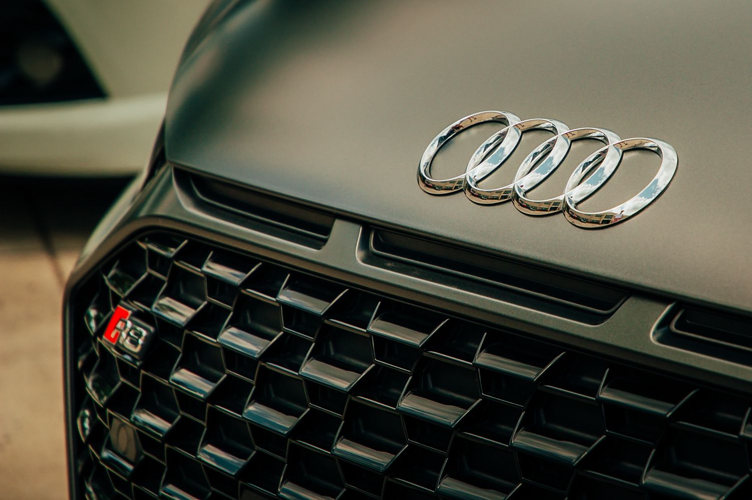 Close-up of chrome Audi four-ring logo on dark gray front grille of luxury car.