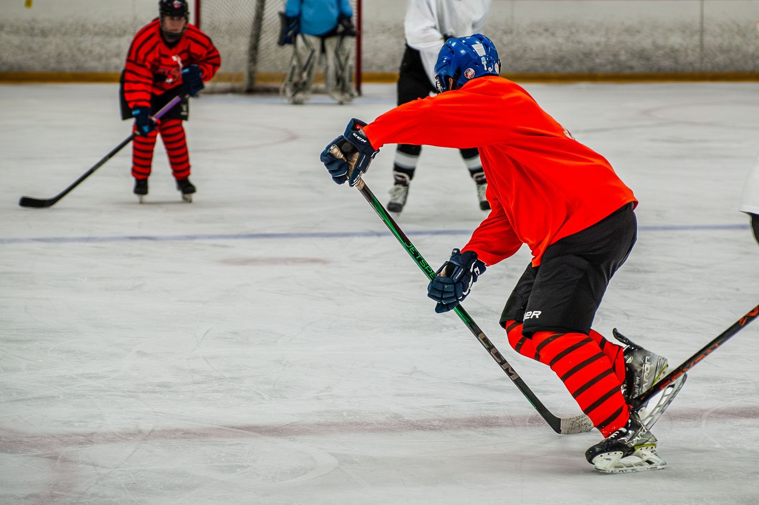Hockey player in red jersey skating aggressively with stick on indoor ice.