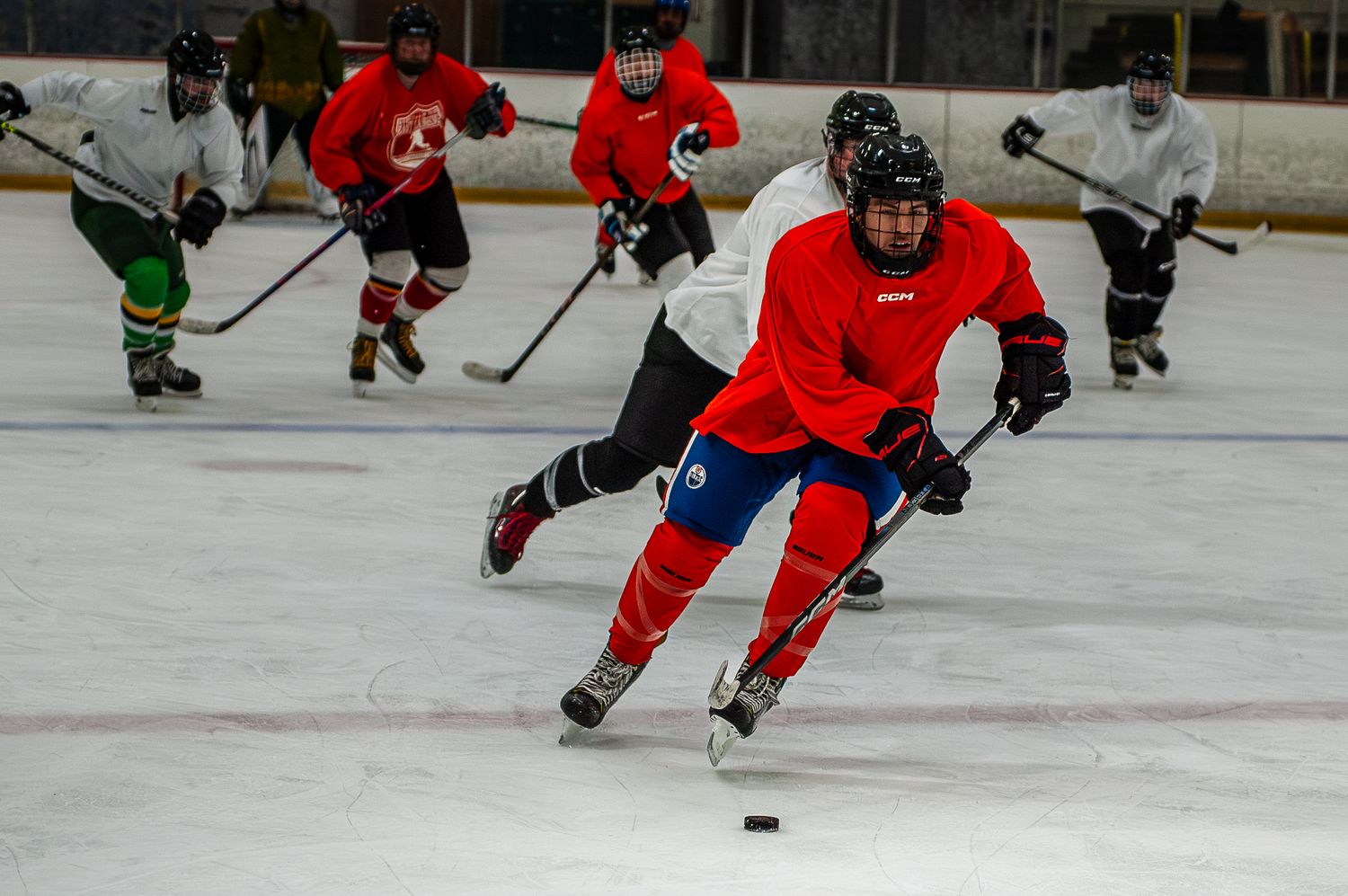 Ice hockey player in red jersey skating fast with puck during game.