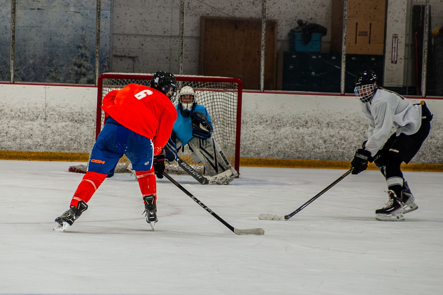 Ice hockey players competing near goal during indoor rink game.