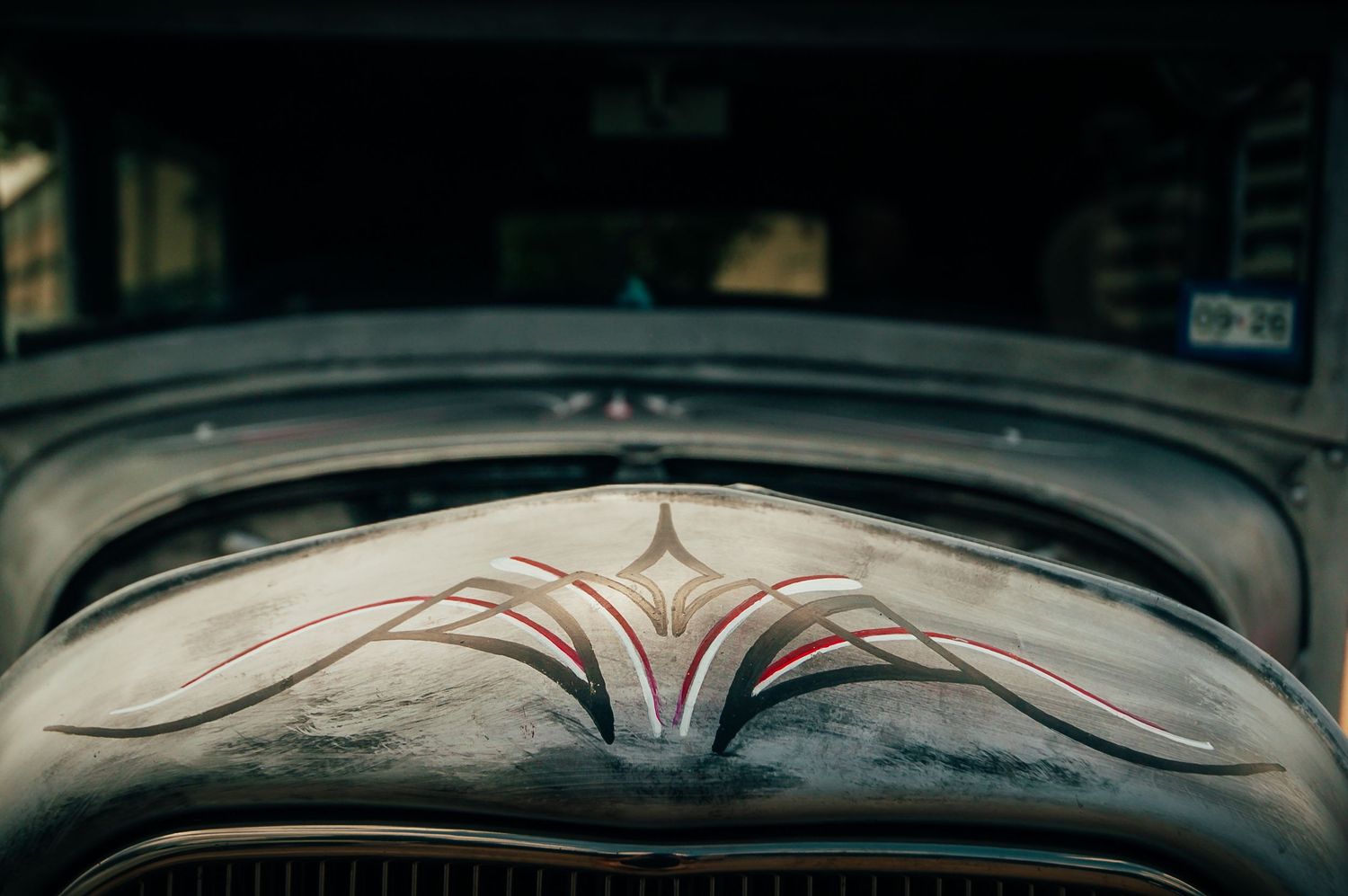 Close-up of intricate custom pinstripe hood ornament design on a vintage patina rat rod.