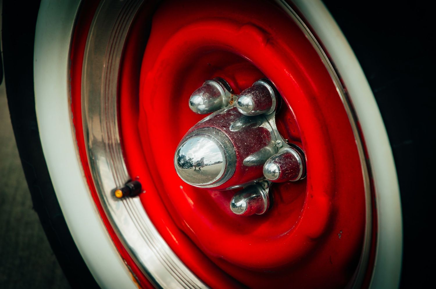 Red and chrome classic car wheel with whitewall tire and polished lug nut center cap.