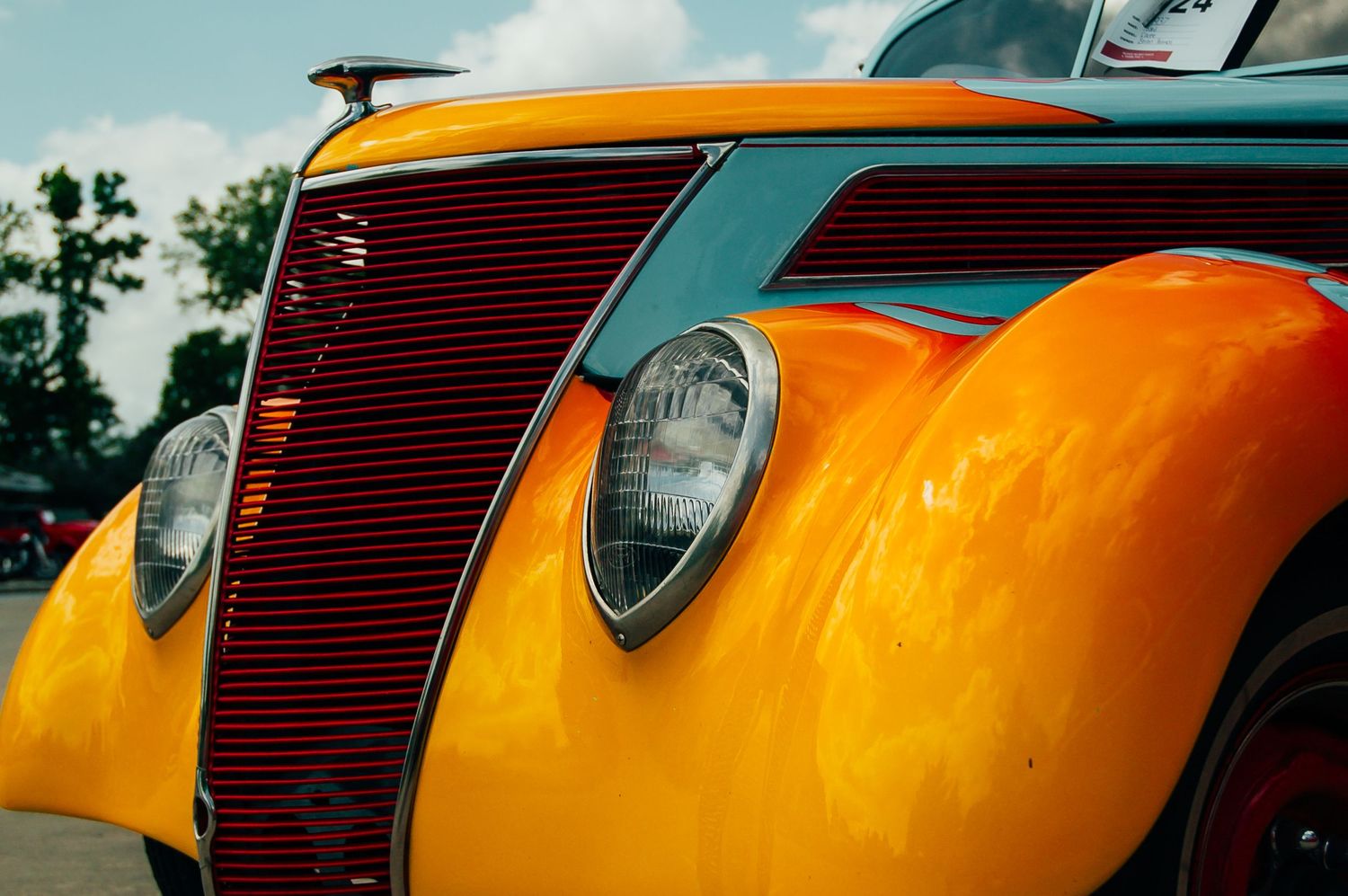 Vintage yellow hot rod with red grille and chrome headlights gleaming at an outdoor car show.