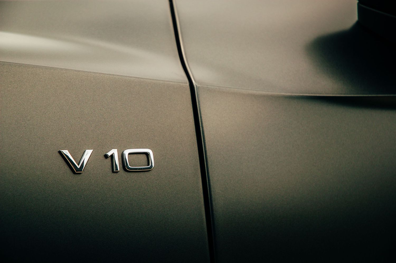 Chrome V10 badge emblem on matte gray Audi R8 supercar body panel close-up.