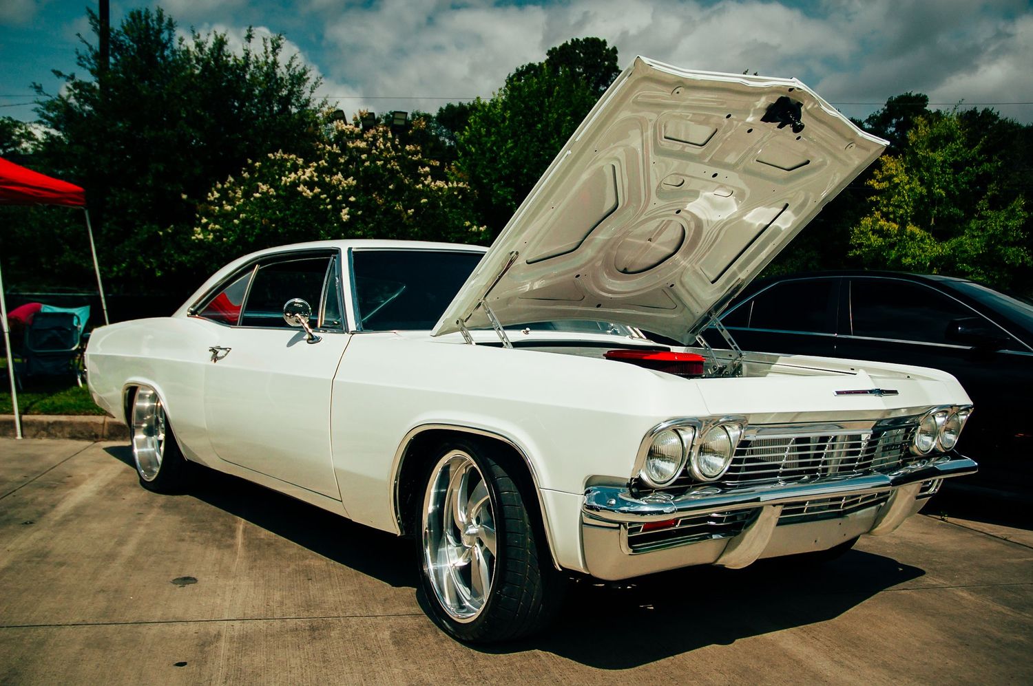 Classic white 1965 Chevrolet Impala with open hood on display at a car show.