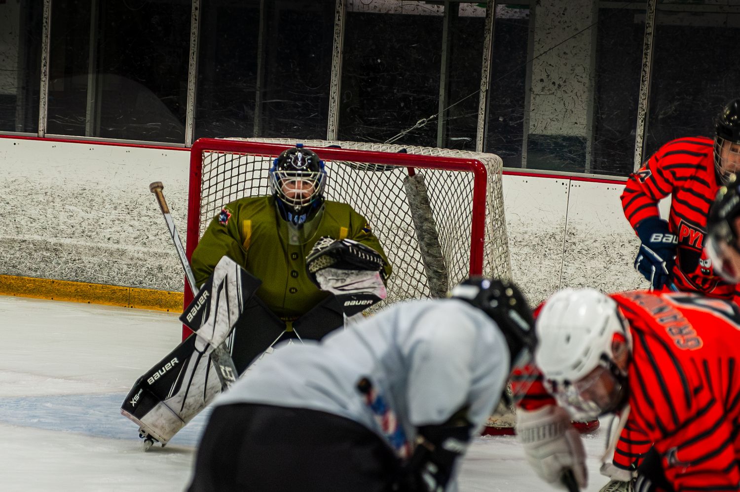 Ice hockey goalie in green jersey guards the net during a competitive game on an indoor rink.