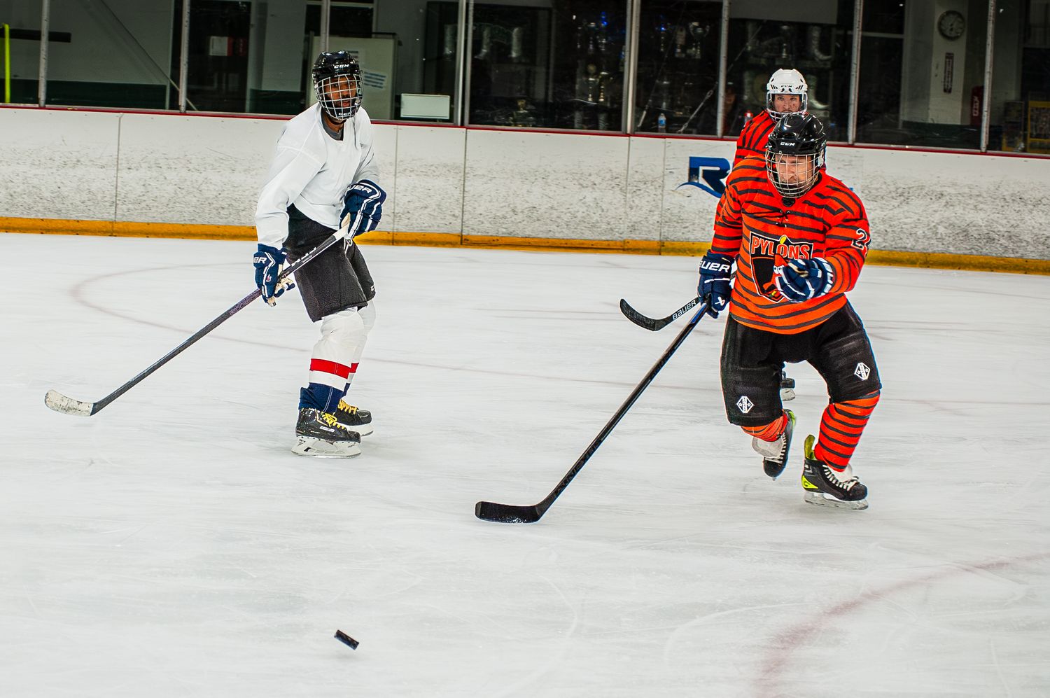 Two ice hockey players chasing puck during indoor rink practice game.