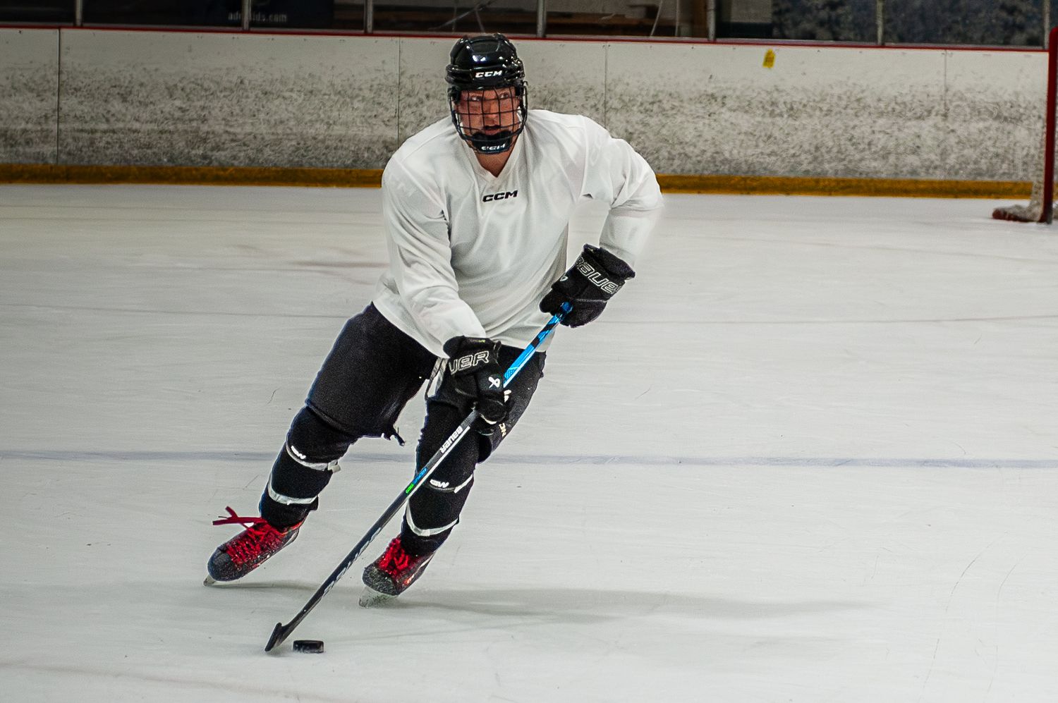 Hockey player in white jersey skating with puck during ice rink practice session.