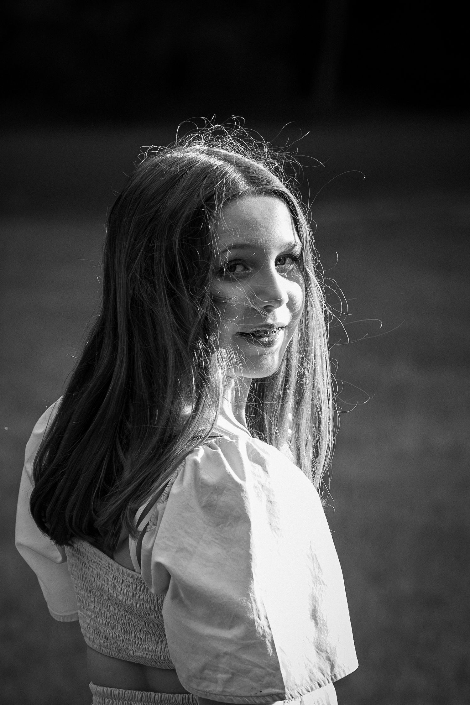 Black and white portrait of a young woman with long hair in a white top standing outdoors.